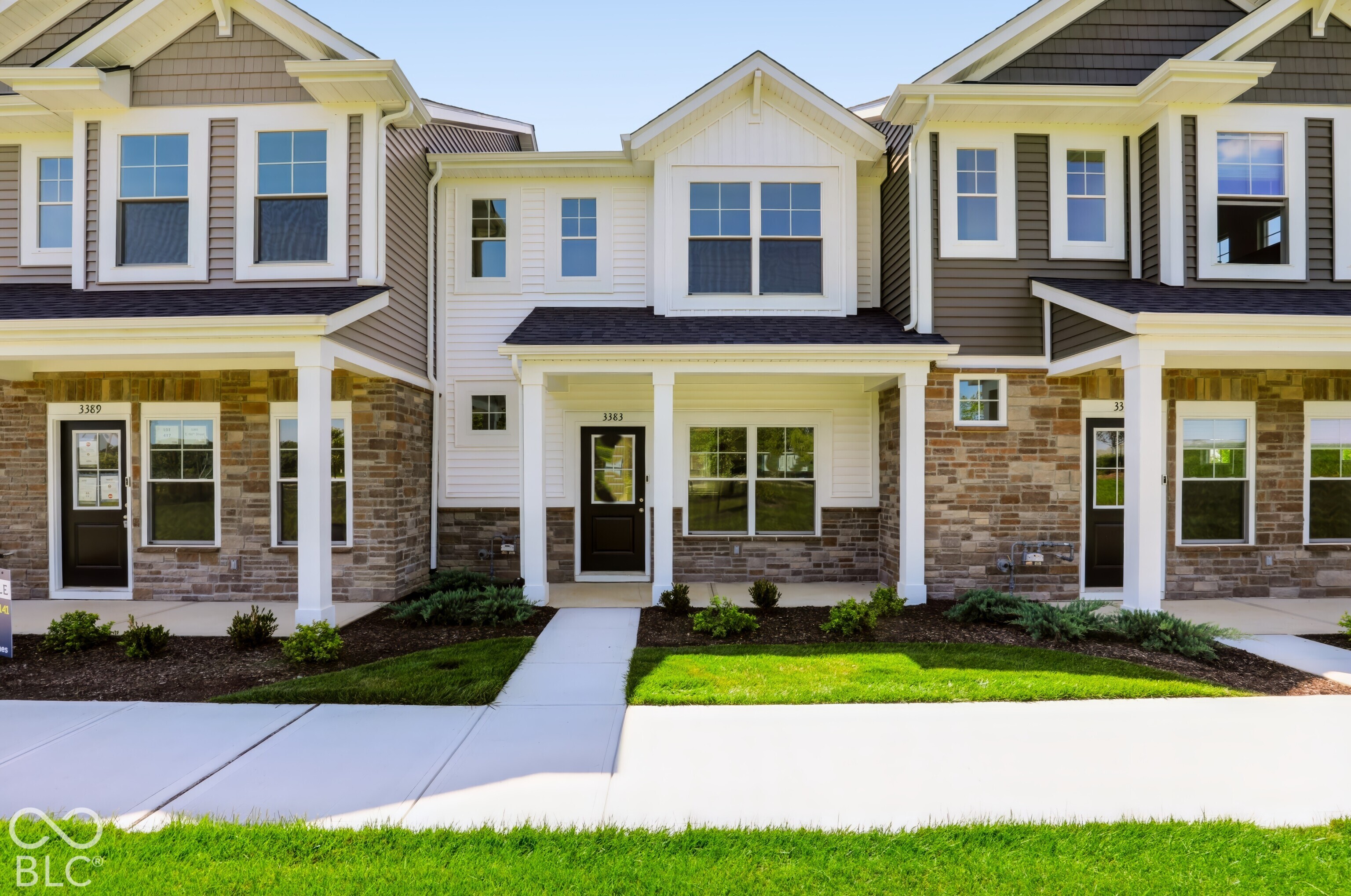 Attached two-story townhomes with stone façades, covered porches, and green front lawns.