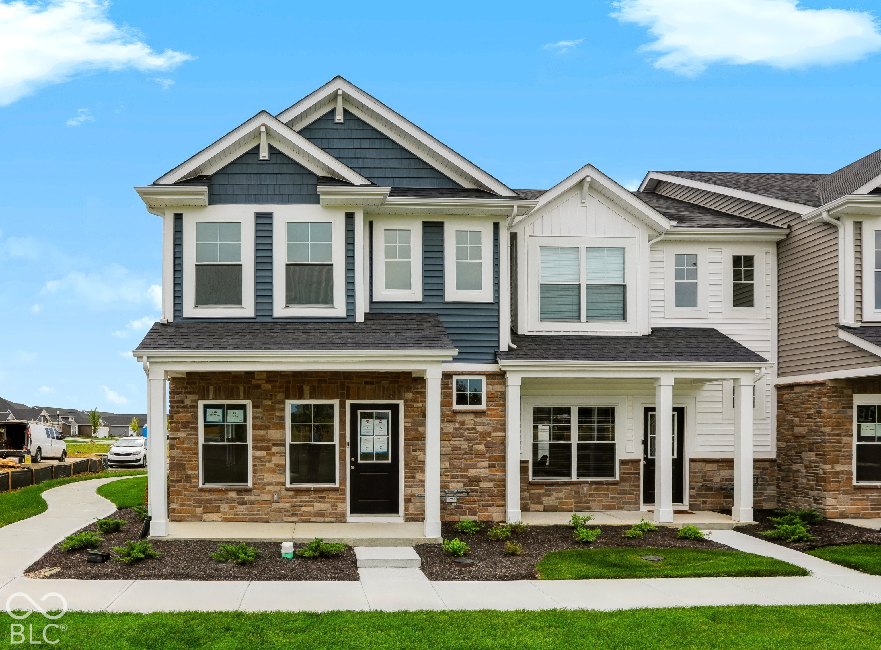 Two-story blue-gray and white home with stone veneer, a covered entry, and landscaped front lawn.