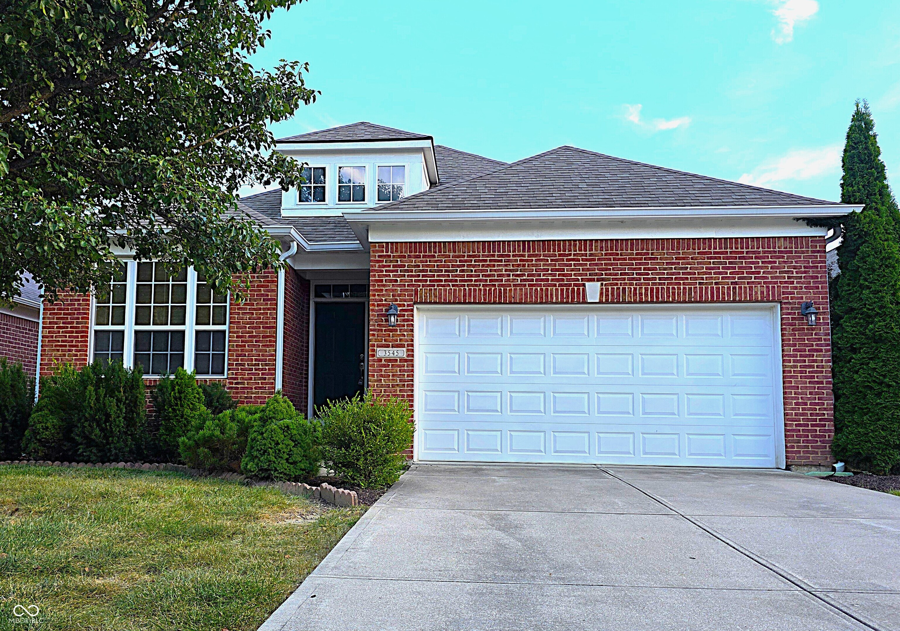 Red brick two-story house with a large white garage door and landscaped front yard.
