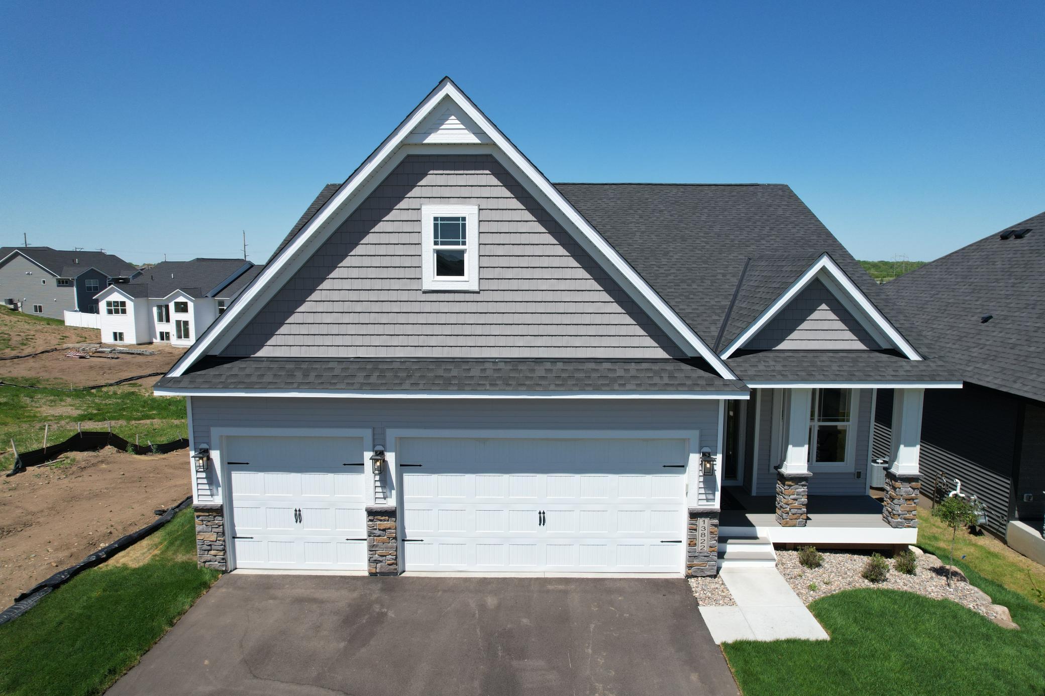 Gray two-story house with steep gables, white trim, and a double garage beside an unfinished lot.