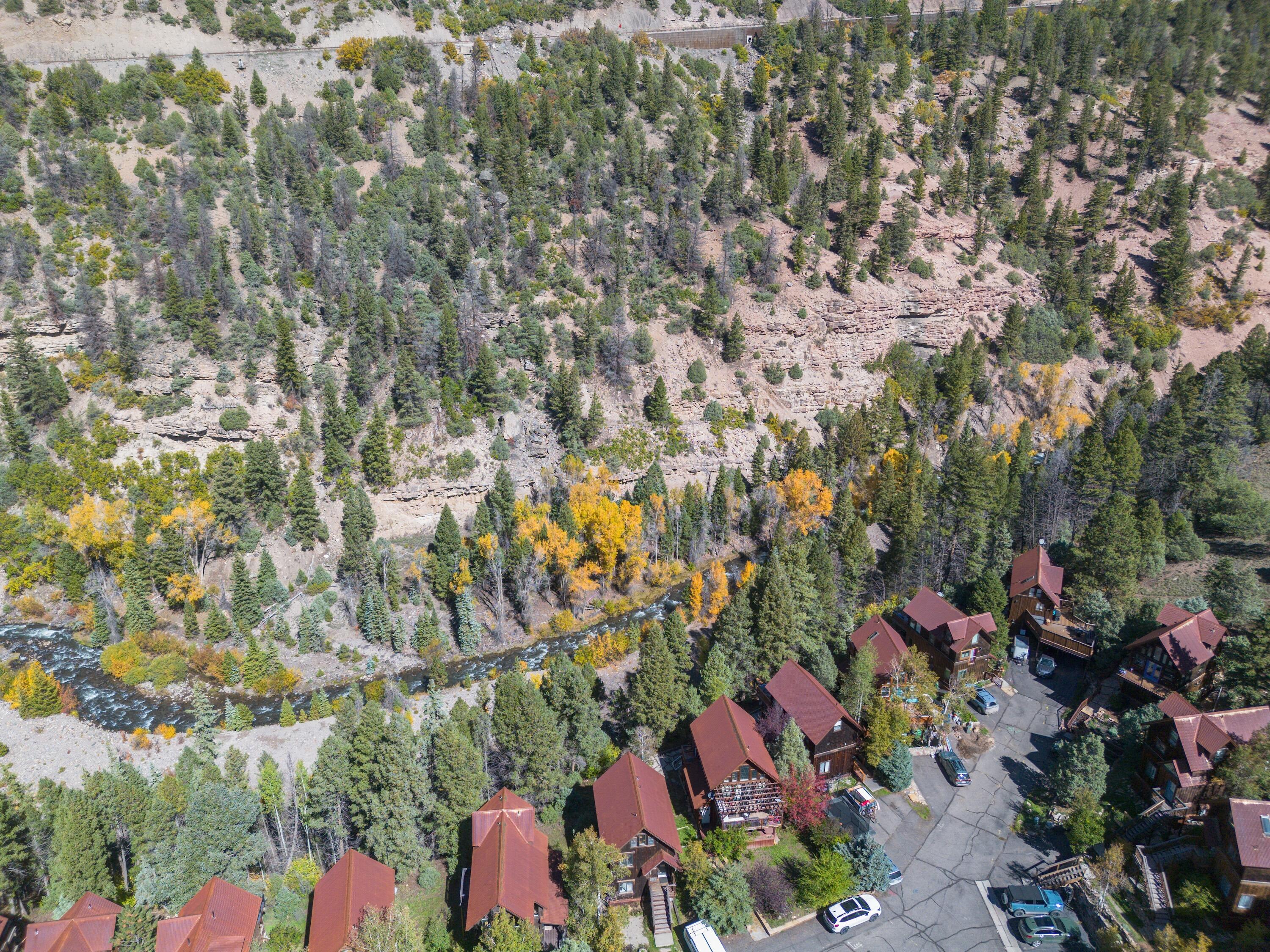 Aerial view of homes along a creek beneath a forested rocky hillside.