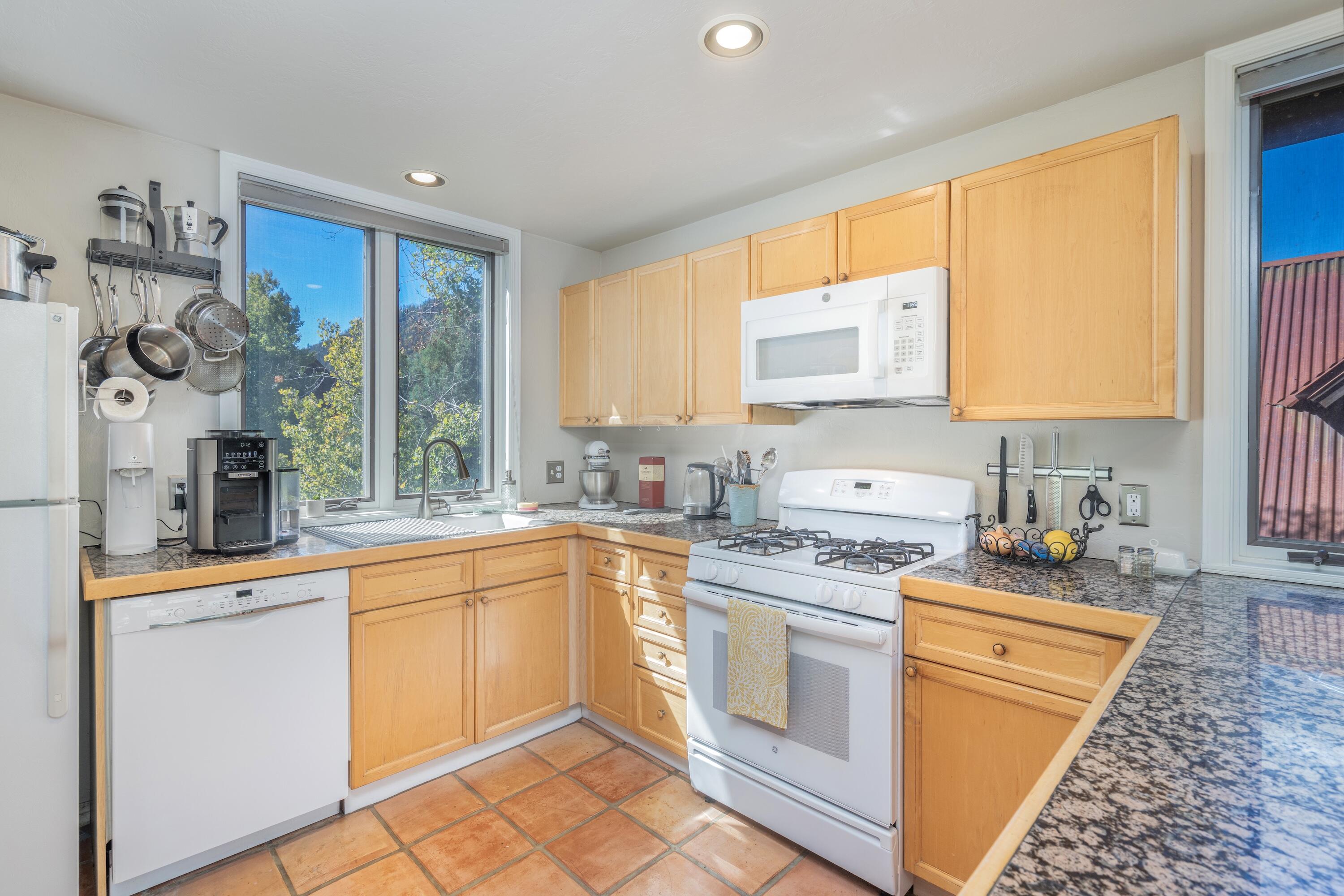 Kitchen with honey-colored cabinets, granite counters, and large windows overlooking trees.