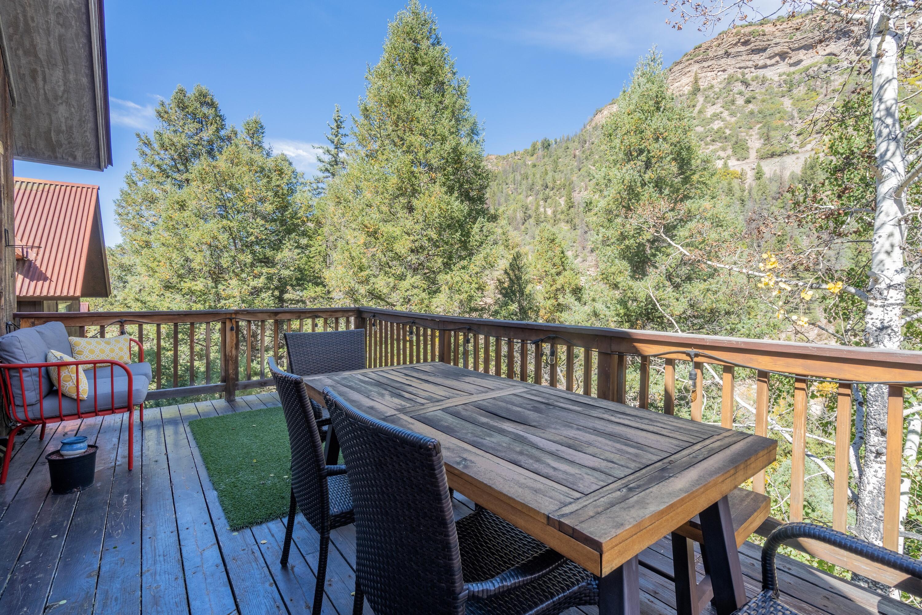 Furnished deck with outdoor dining table overlooking a wooded mountain slope.