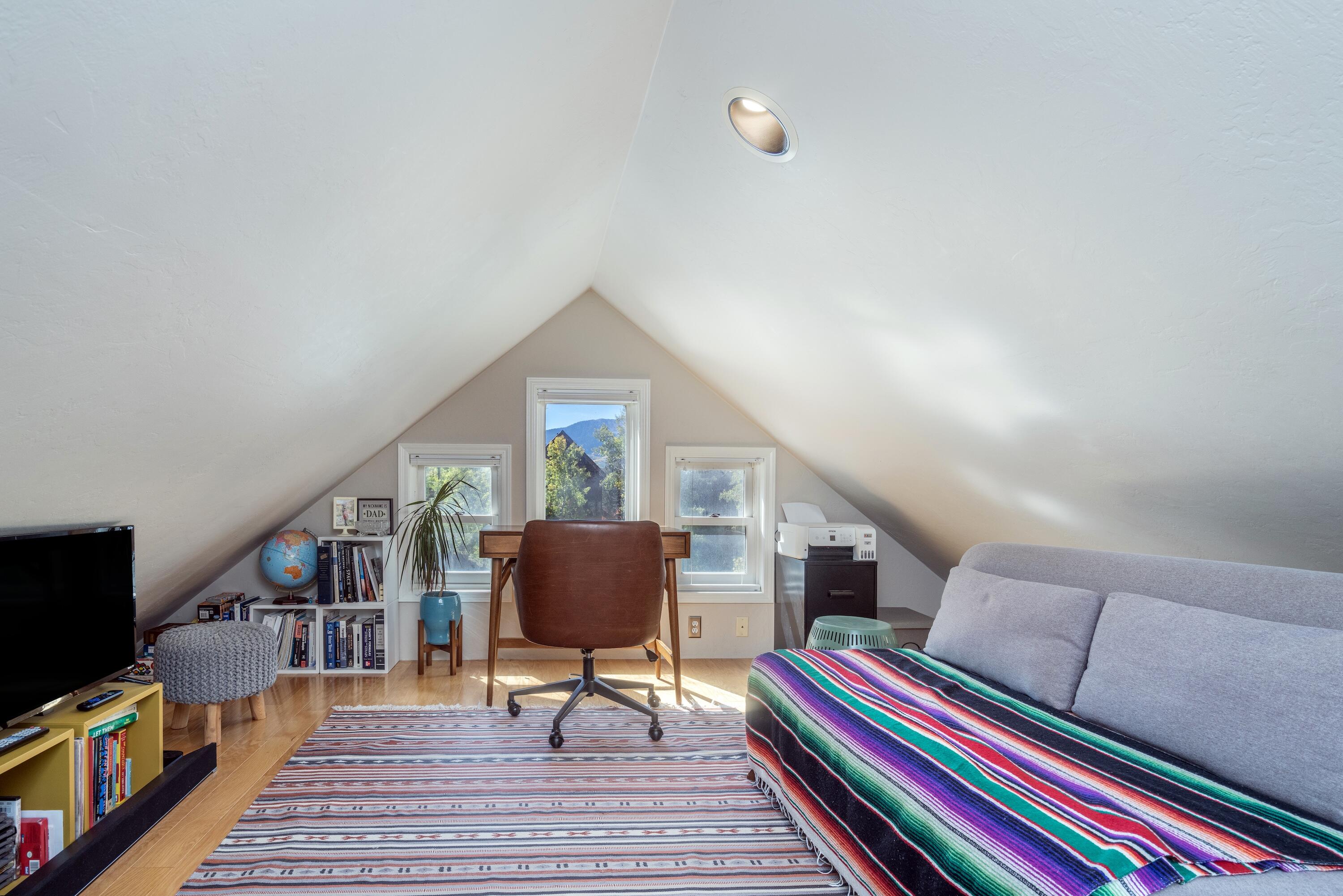 Furnished attic office and sitting area with sloped ceilings, a desk, sofa, and mountain views through the windows.