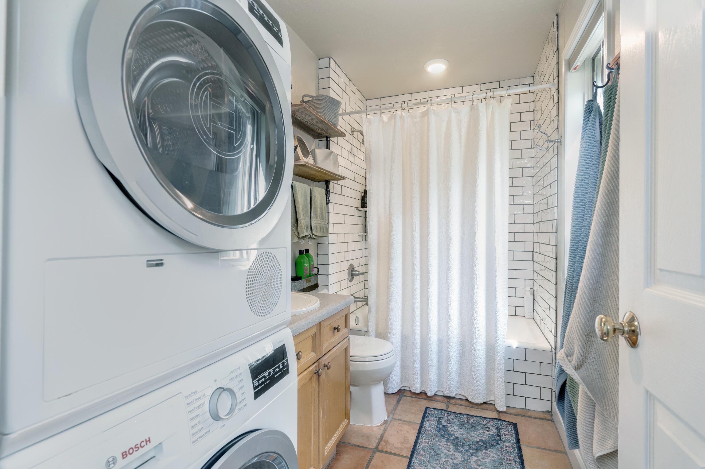Bathroom with a white subway-tile shower, wooden vanity, and stacked washer and dryer.