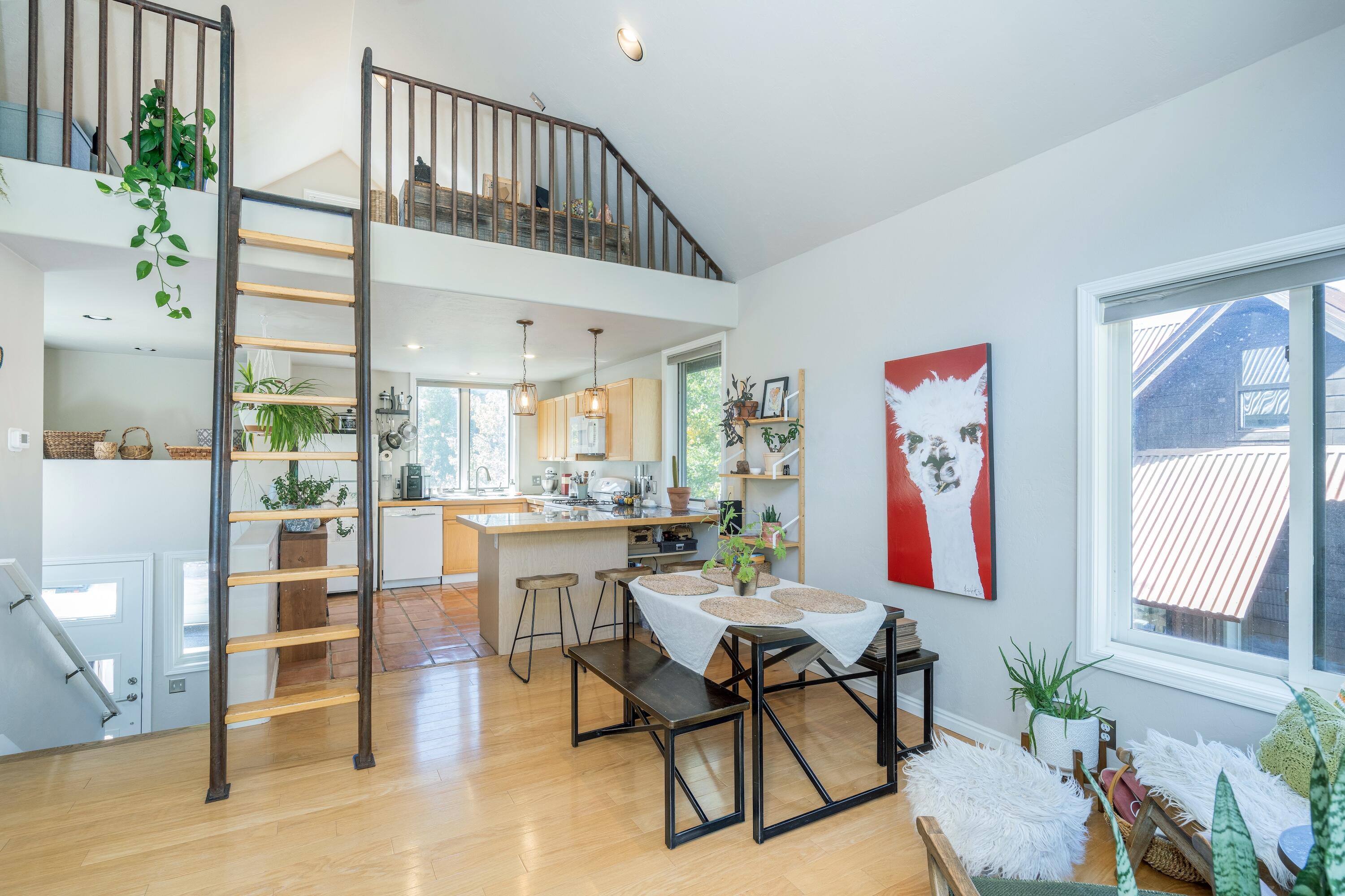 Open kitchen and dining area with a loft, ladder, and large windows.