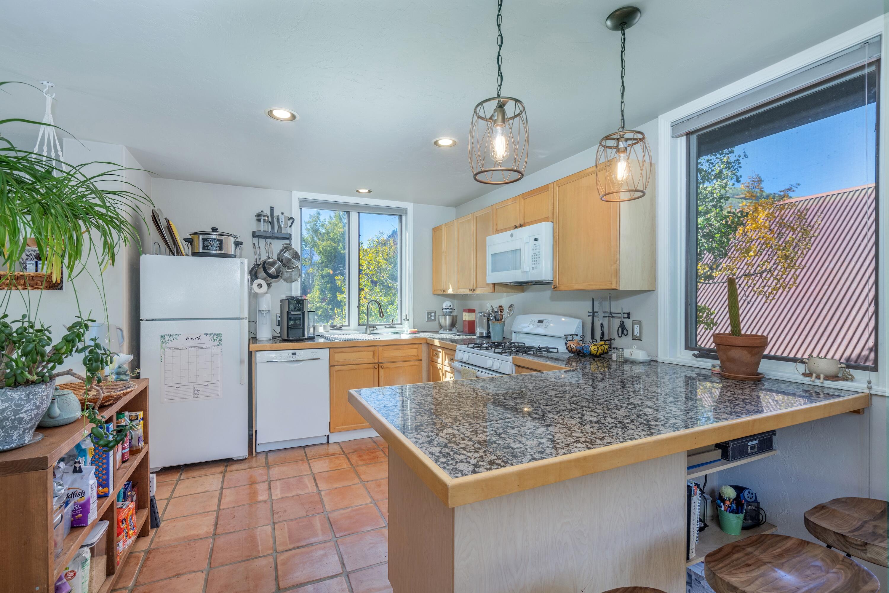 Kitchen with granite island, honey-colored cabinets, terracotta tile, and windows overlooking autumn trees.