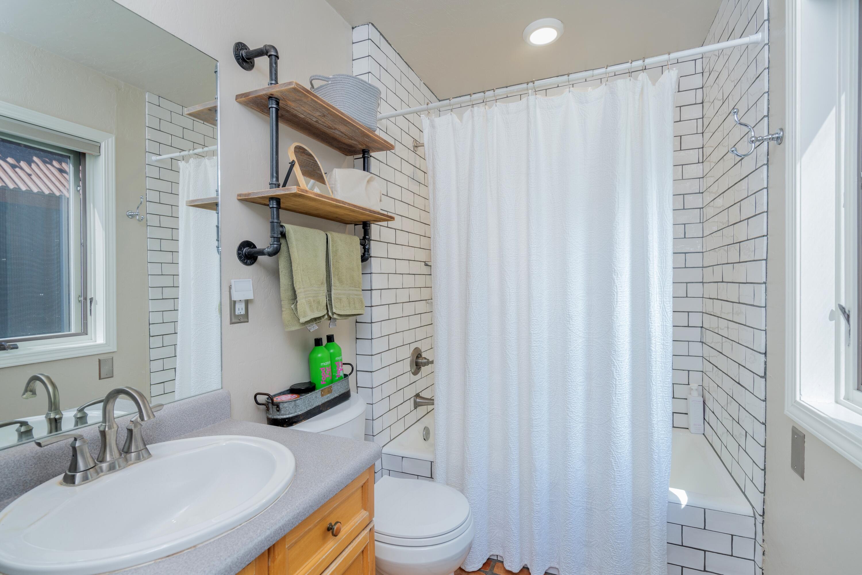 Bathroom with white subway tile, a shower curtain, and a wood-and-pipe towel shelf.
