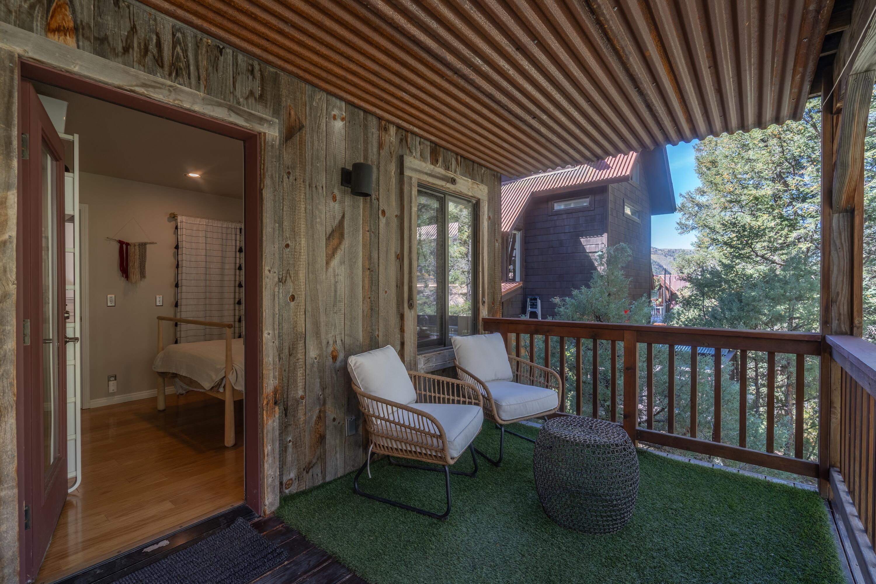 Covered balcony with cushioned chairs, artificial turf, and views of surrounding trees.