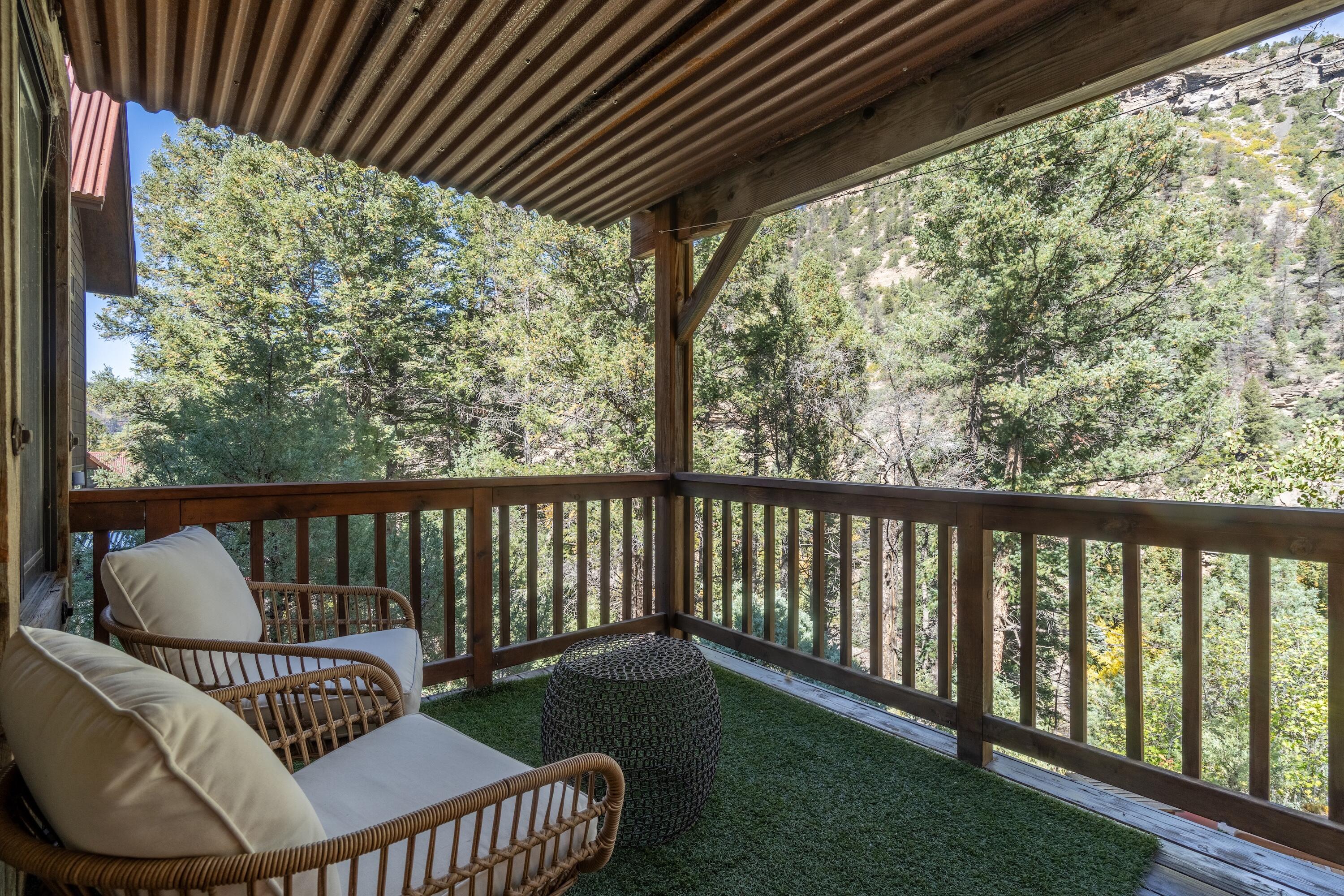 Covered wood balcony with cushioned chairs overlooking a forested hillside.