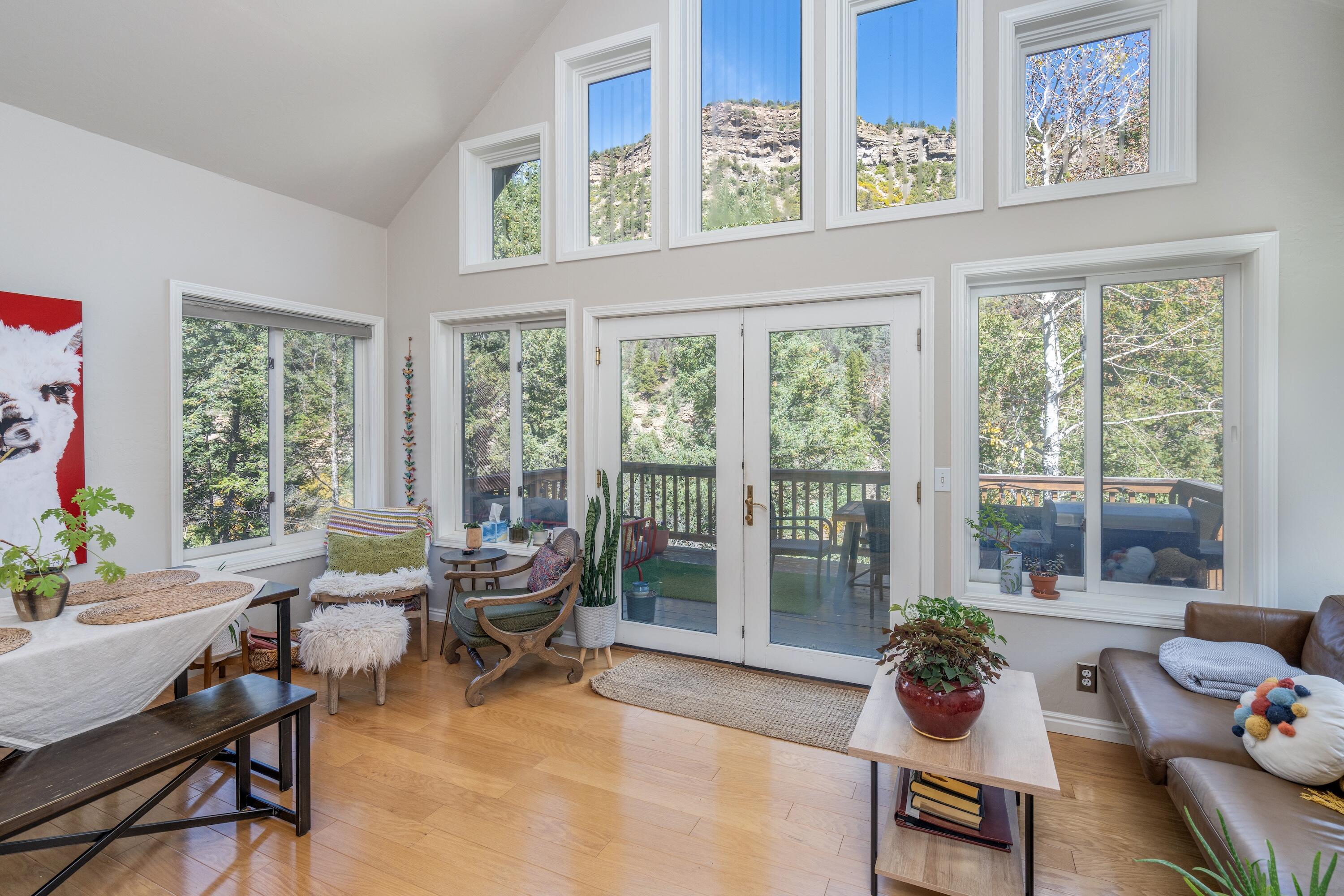Bright living area with high windows overlooking wooded slopes and a deck.