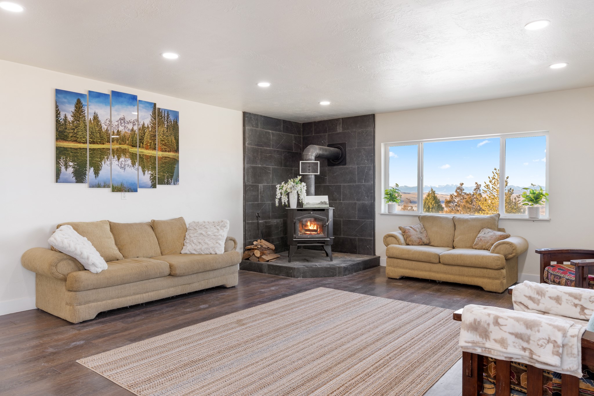 Living room with a wood-burning stove, tan sofas, and mountain views through a wide window.
