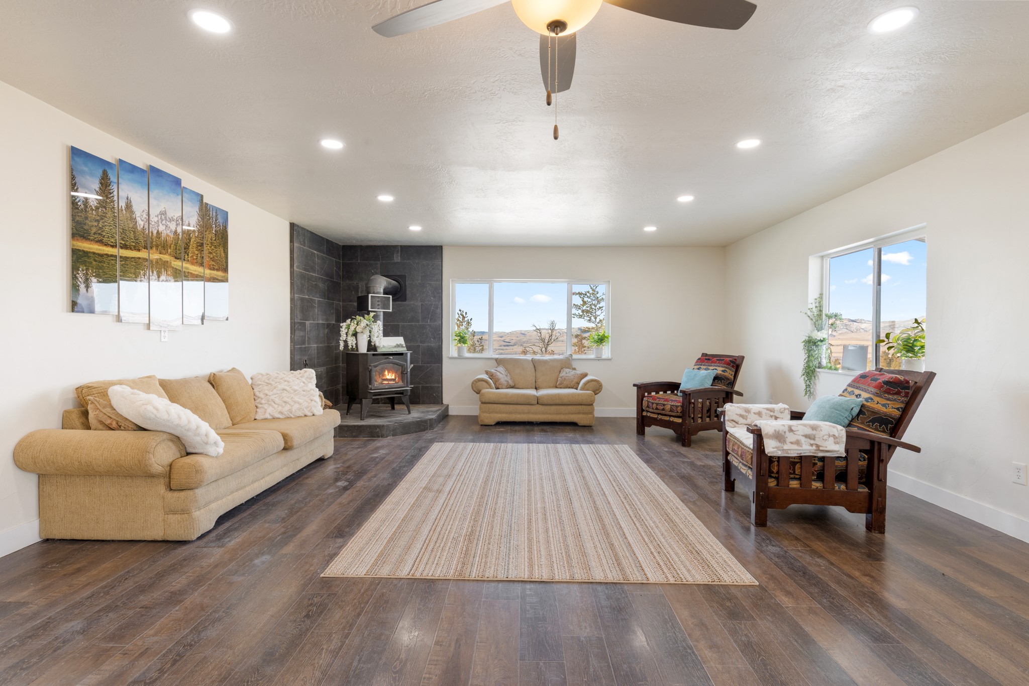 Living room with a tiled wood-stove fireplace, beige sectional, and patterned armchairs beside large windows.