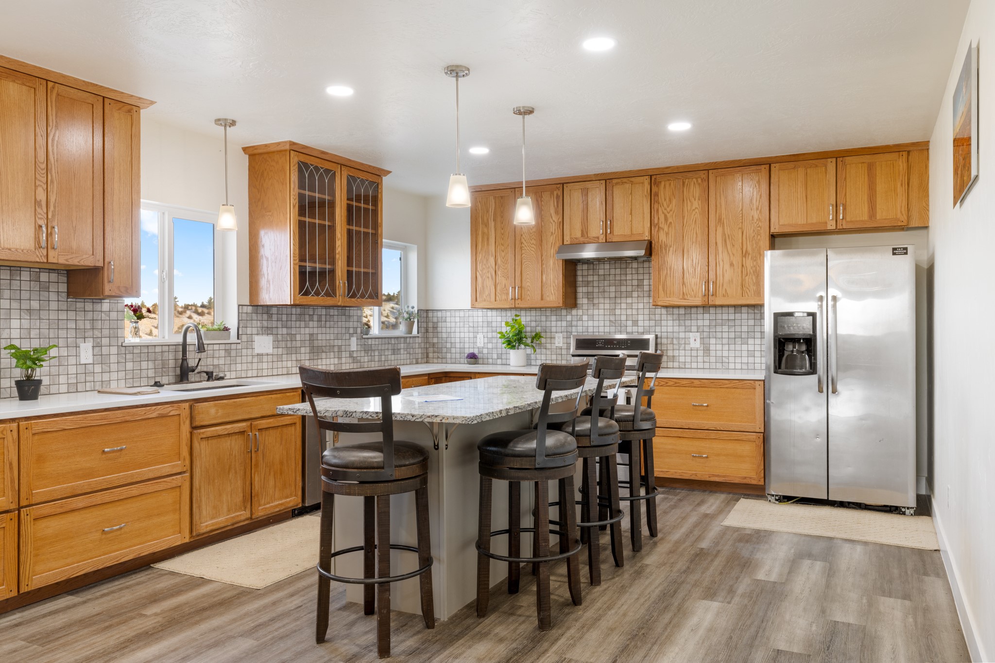 Kitchen with warm wood cabinetry, tiled backsplash, stainless appliances, and a granite island with bar stools.