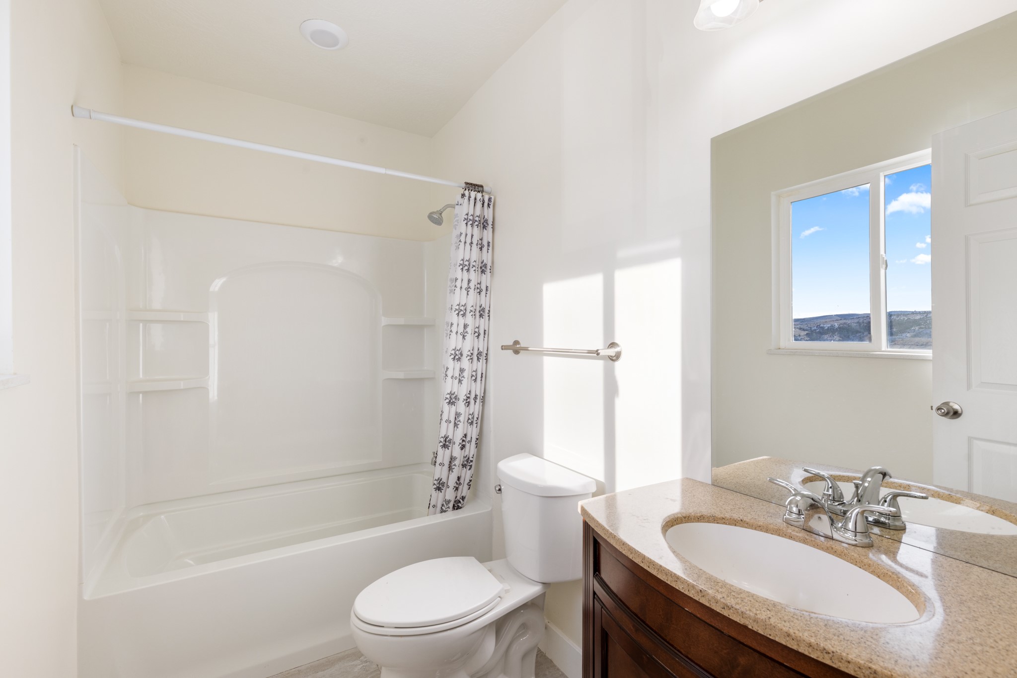 Bathroom with a tub-shower, dark wood vanity, and window overlooking a distant hillside.