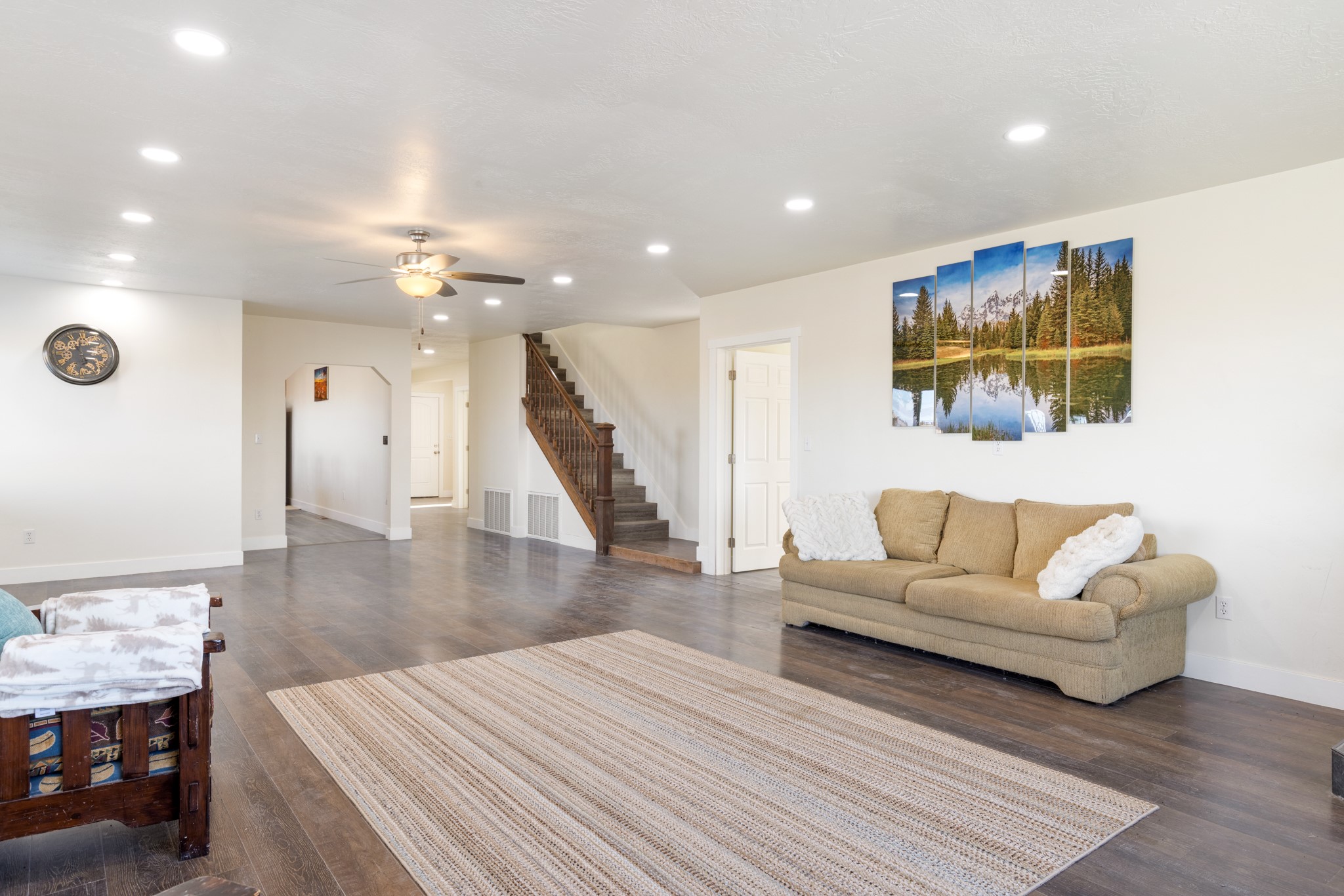 Living room with a tan sofa, woven rug, and wooden staircase.