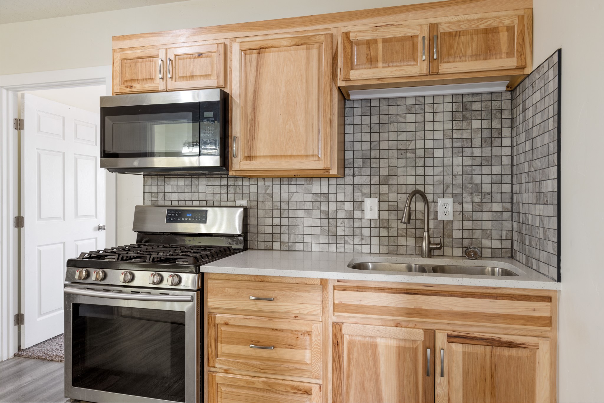 Kitchen with natural wood cabinets, gray tile backsplash, stainless steel appliances, and a double-basin sink.