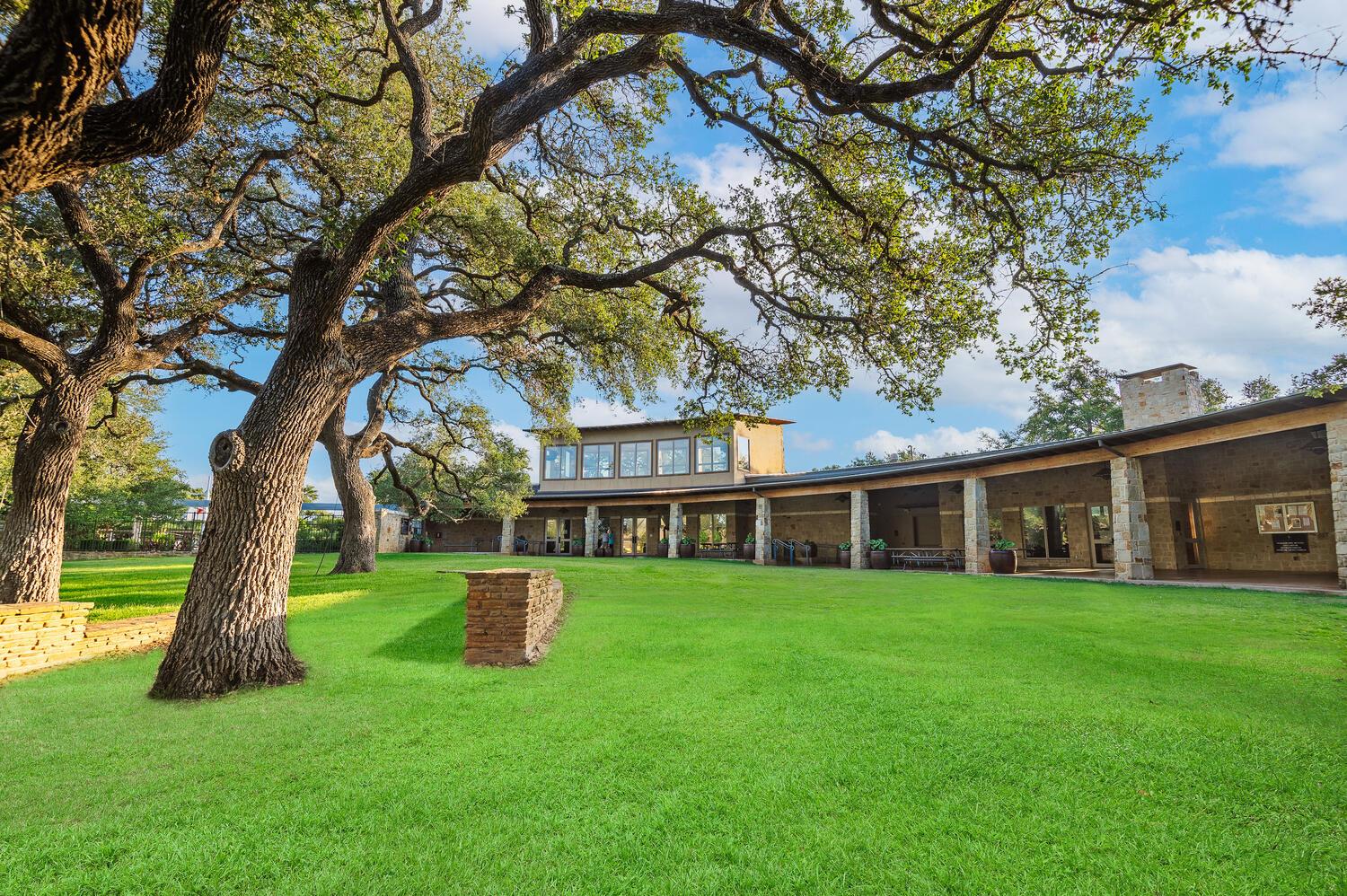 Stone house with a long covered patio beneath sprawling oak trees and a broad green lawn.