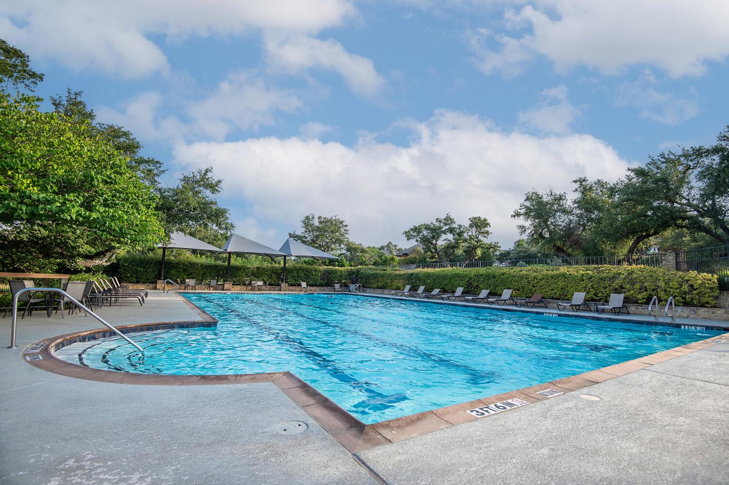 Community swimming pool with turquoise water, shaded seating, and lounge chairs beneath mature trees.