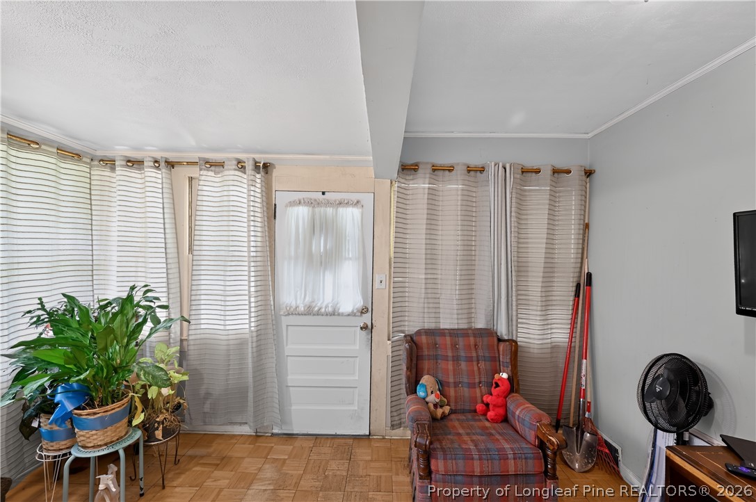Furnished room with a white door, plaid armchair, striped curtains, and potted plants.