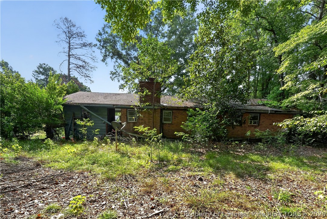 Single-story brick house behind an overgrown, wooded yard, with a satellite dish.