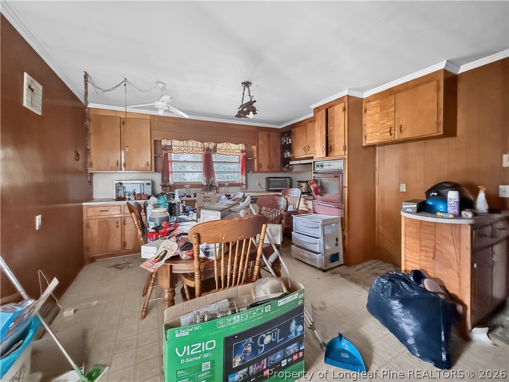 Cluttered kitchen with wood-paneled walls, wooden cabinets, and a dining table surrounded by chairs.