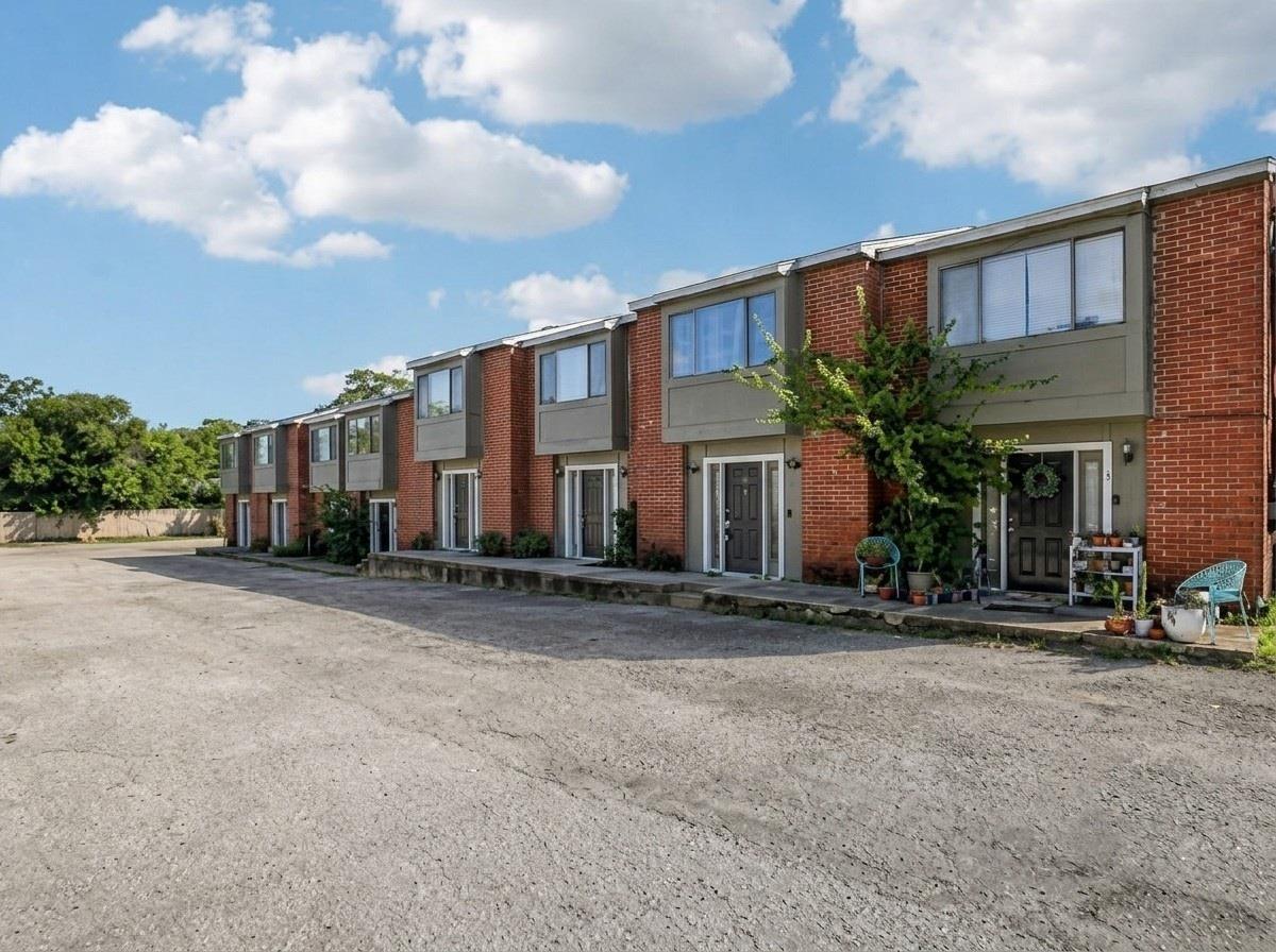 Brick townhouses with gray upper facades, front patios, and a broad paved parking area.