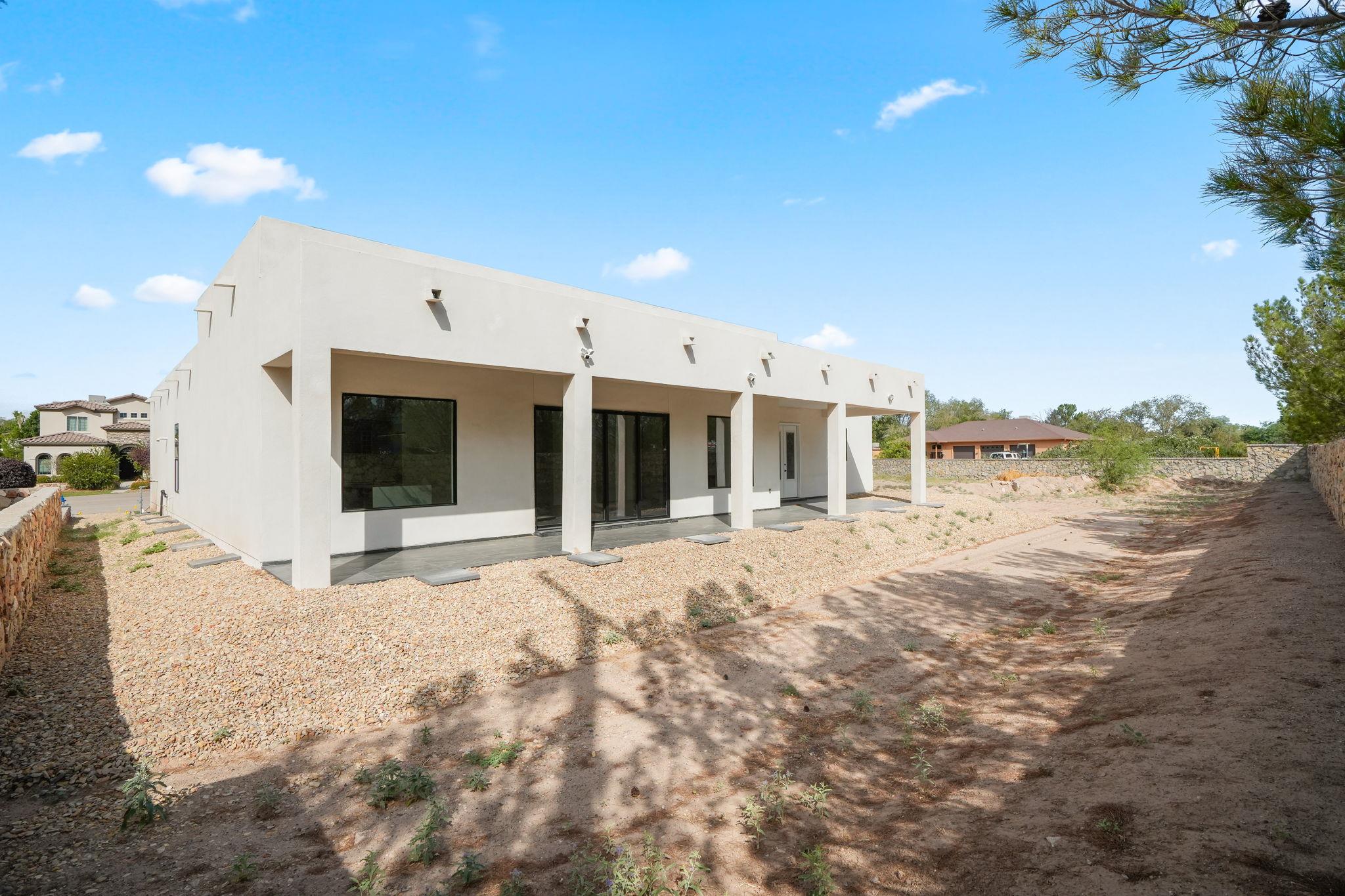 Modern white stucco home with a long covered patio and a bare gravel yard.