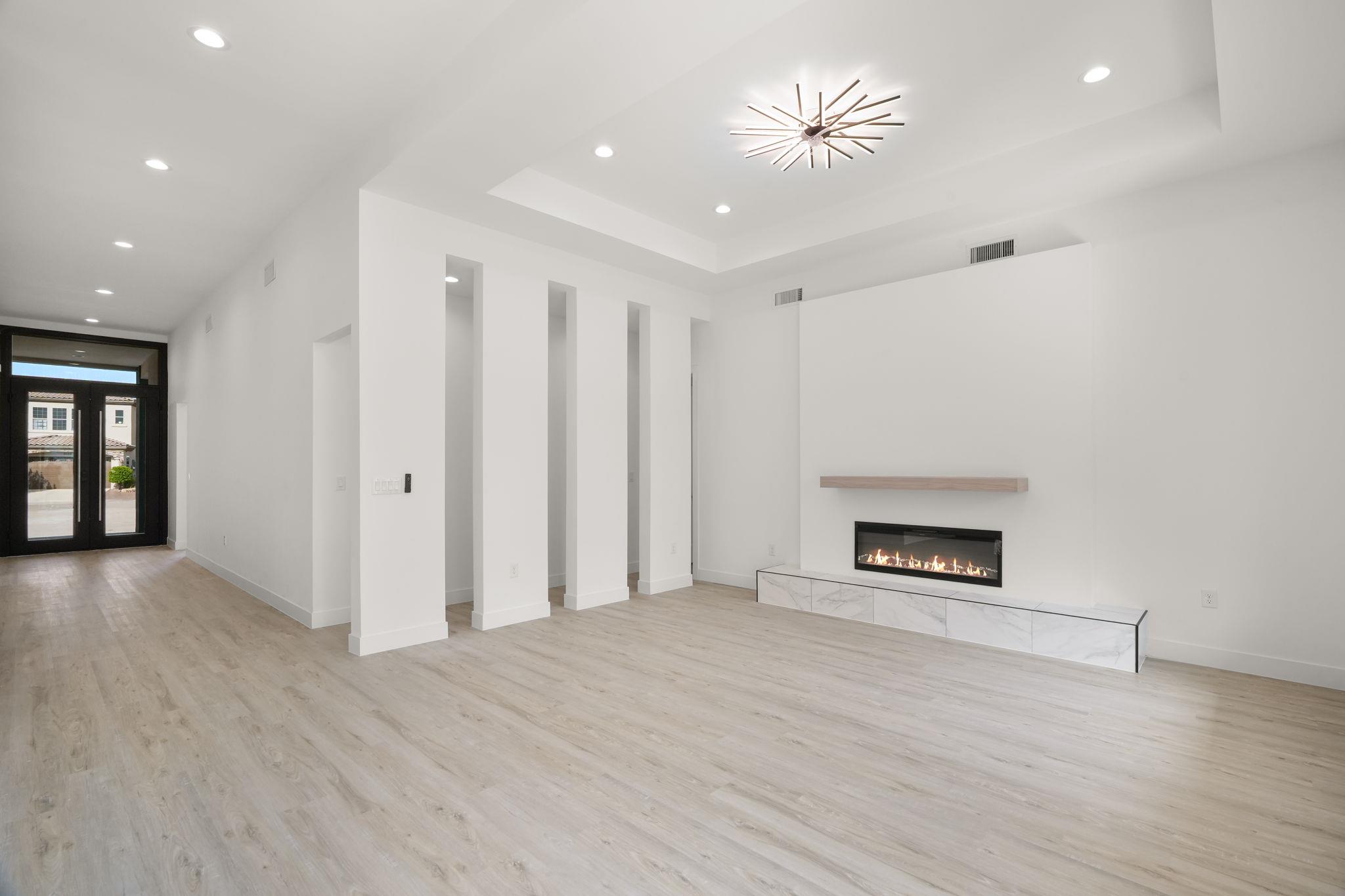 Unfurnished modern living room with light wood floors, a high ceiling, and a linear fireplace.