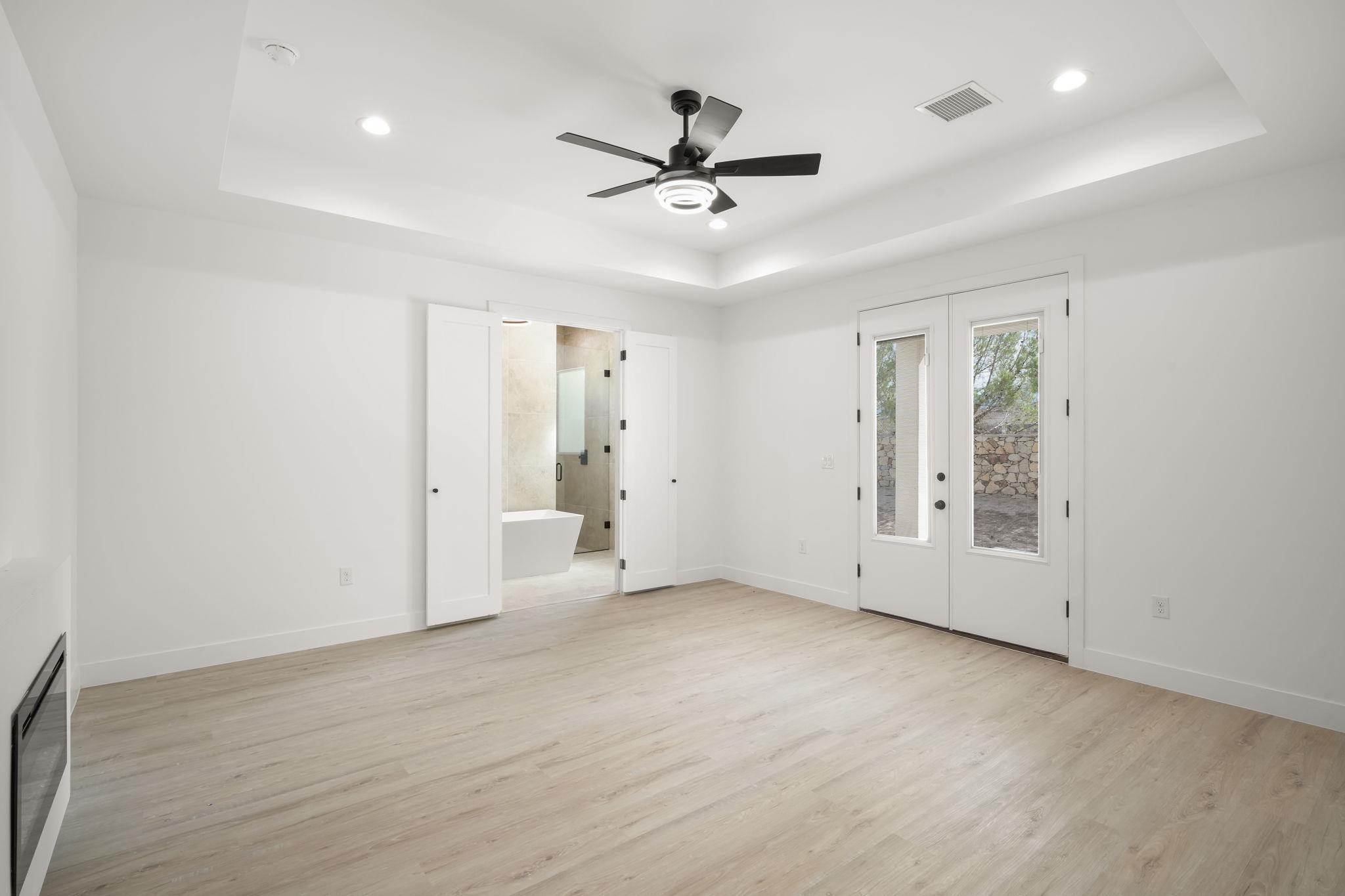 Empty room with a black ceiling fan, patio doors, and an adjoining bathroom with a freestanding tub.