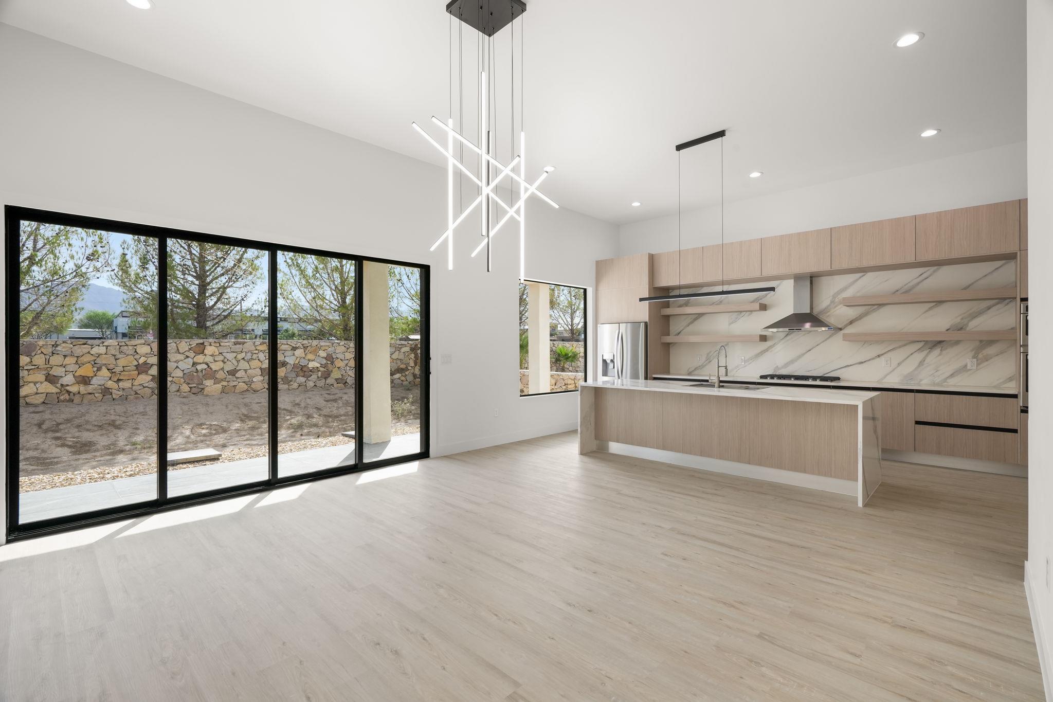 Modern kitchen with a large island, veined stone backsplash, and sliding glass doors to a stone-walled garden.