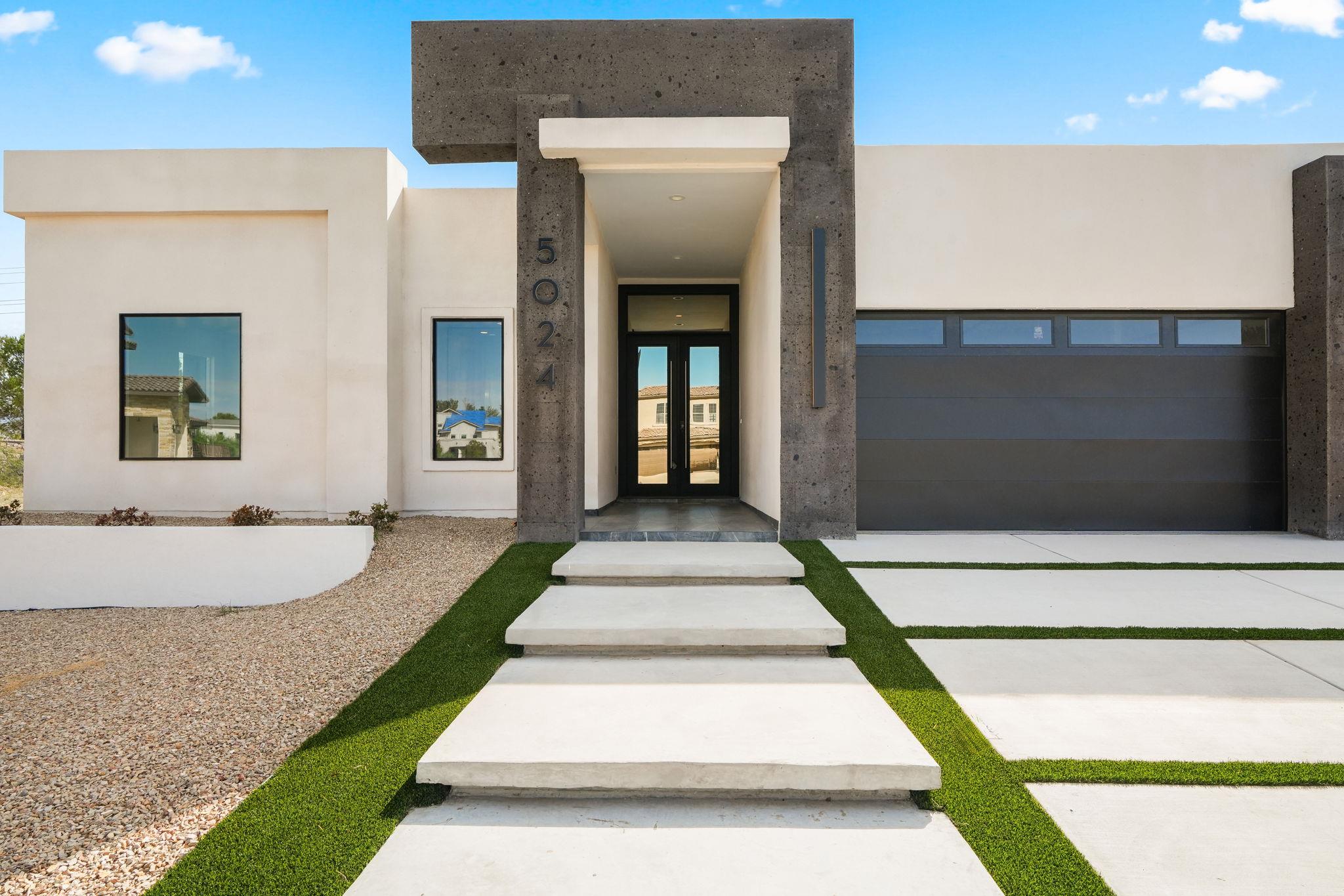 Modern home exterior with a dark stone entry surround, recessed glass door, and lawn-striped concrete walkway.