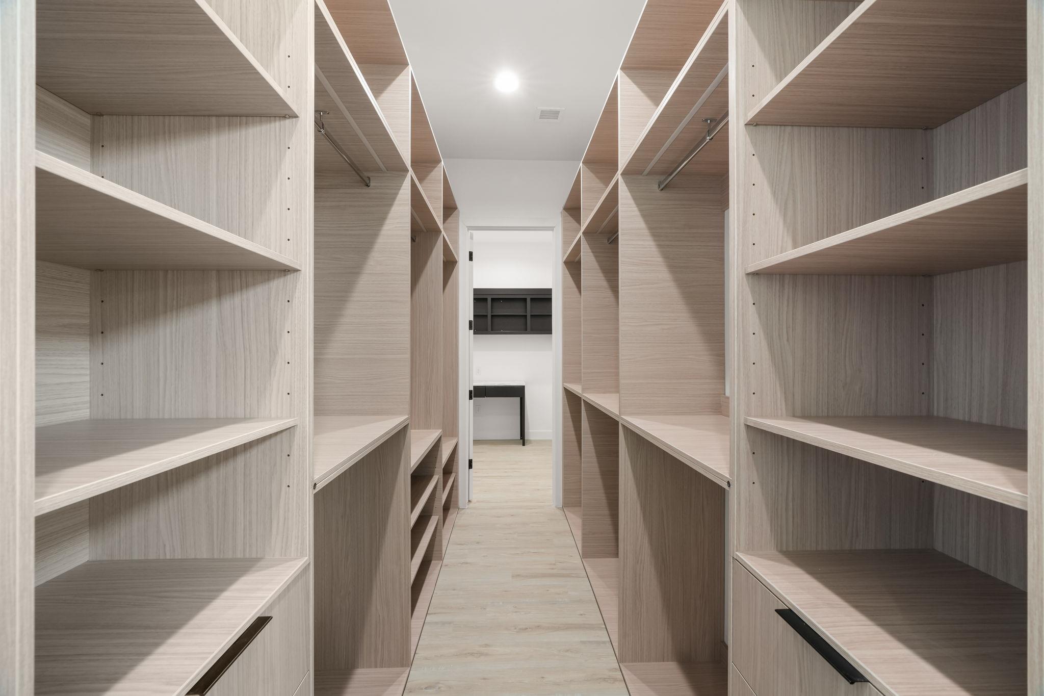 Walk-in closet with light wood built-in shelves and hanging rods.