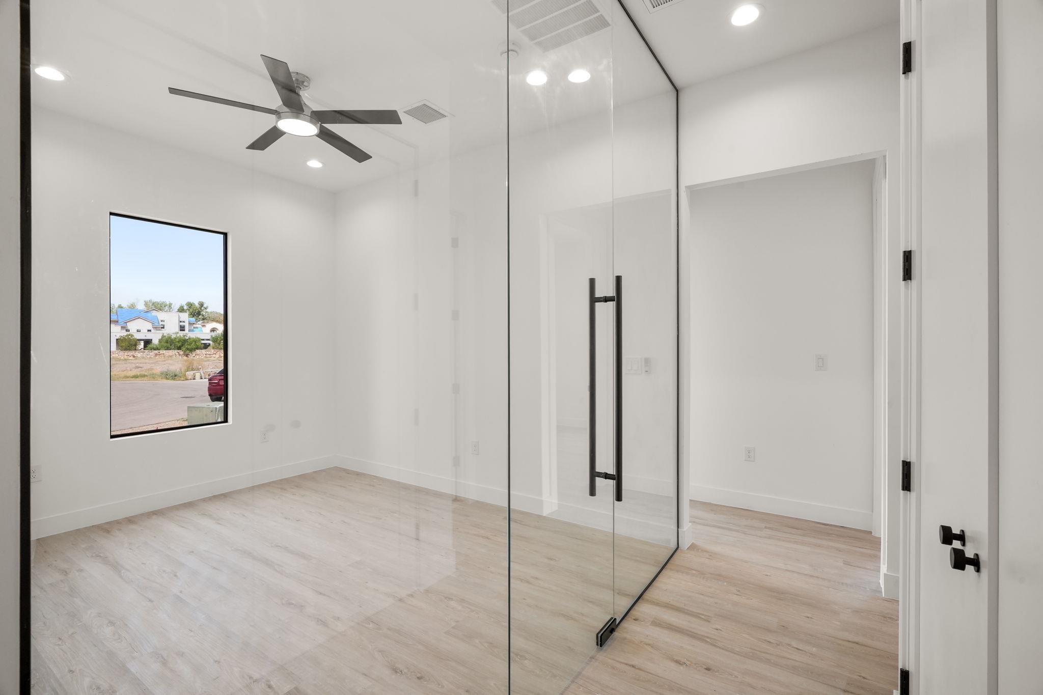 Vacant room with a glass partition, pale wood-look flooring, ceiling fan, and street-facing window.