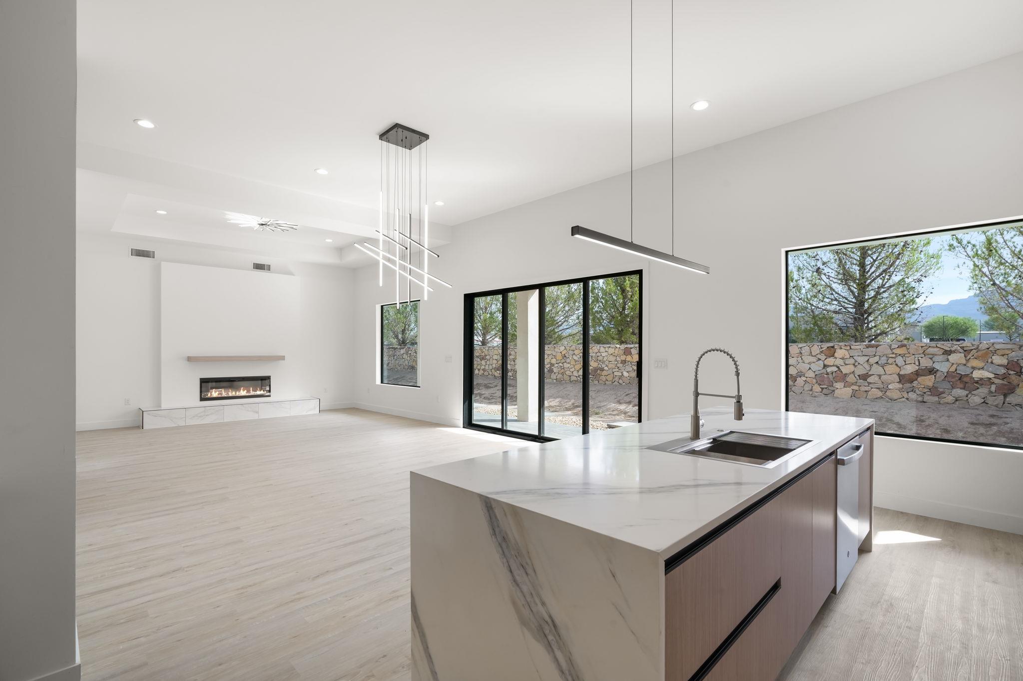 Open-plan kitchen with a marble island, fireplace, and windows overlooking trees and distant mountains.