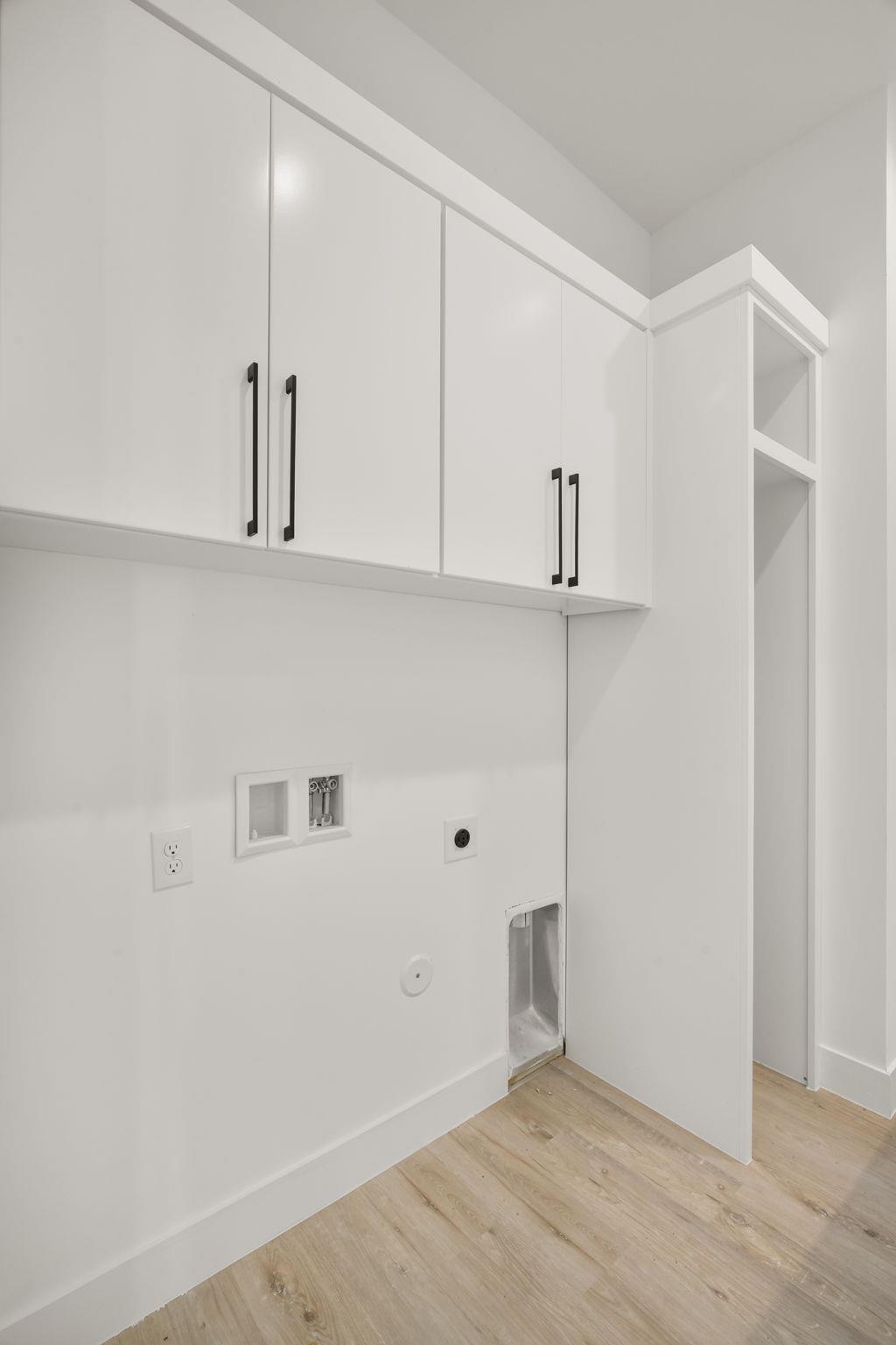 Laundry room with white cabinets, washer hookups, and light wood-look flooring.