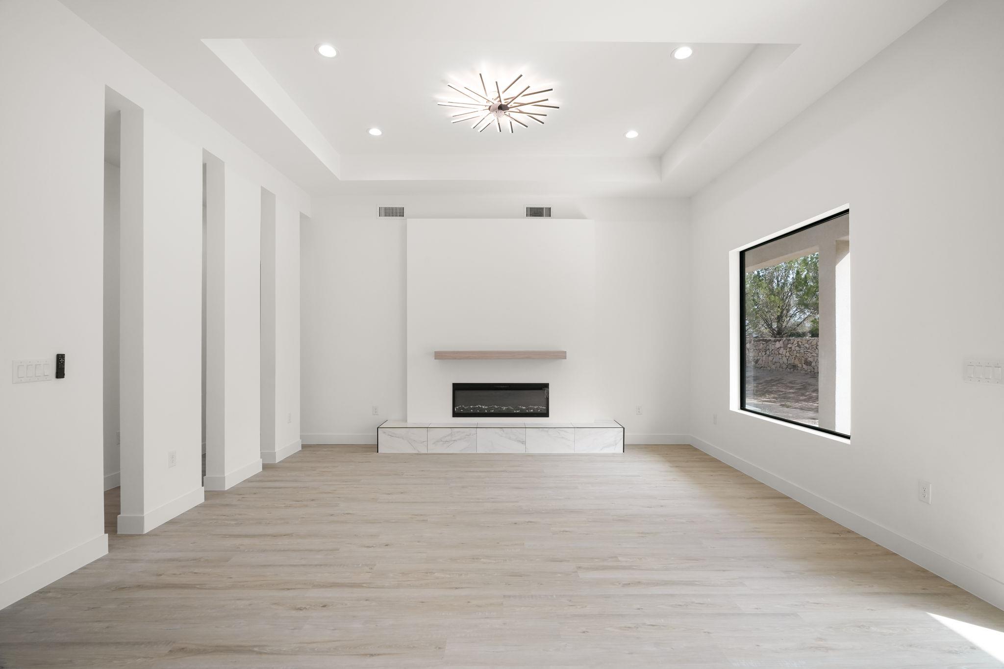 Vacant modern living room with pale wood floors, a linear fireplace, and a large picture window.