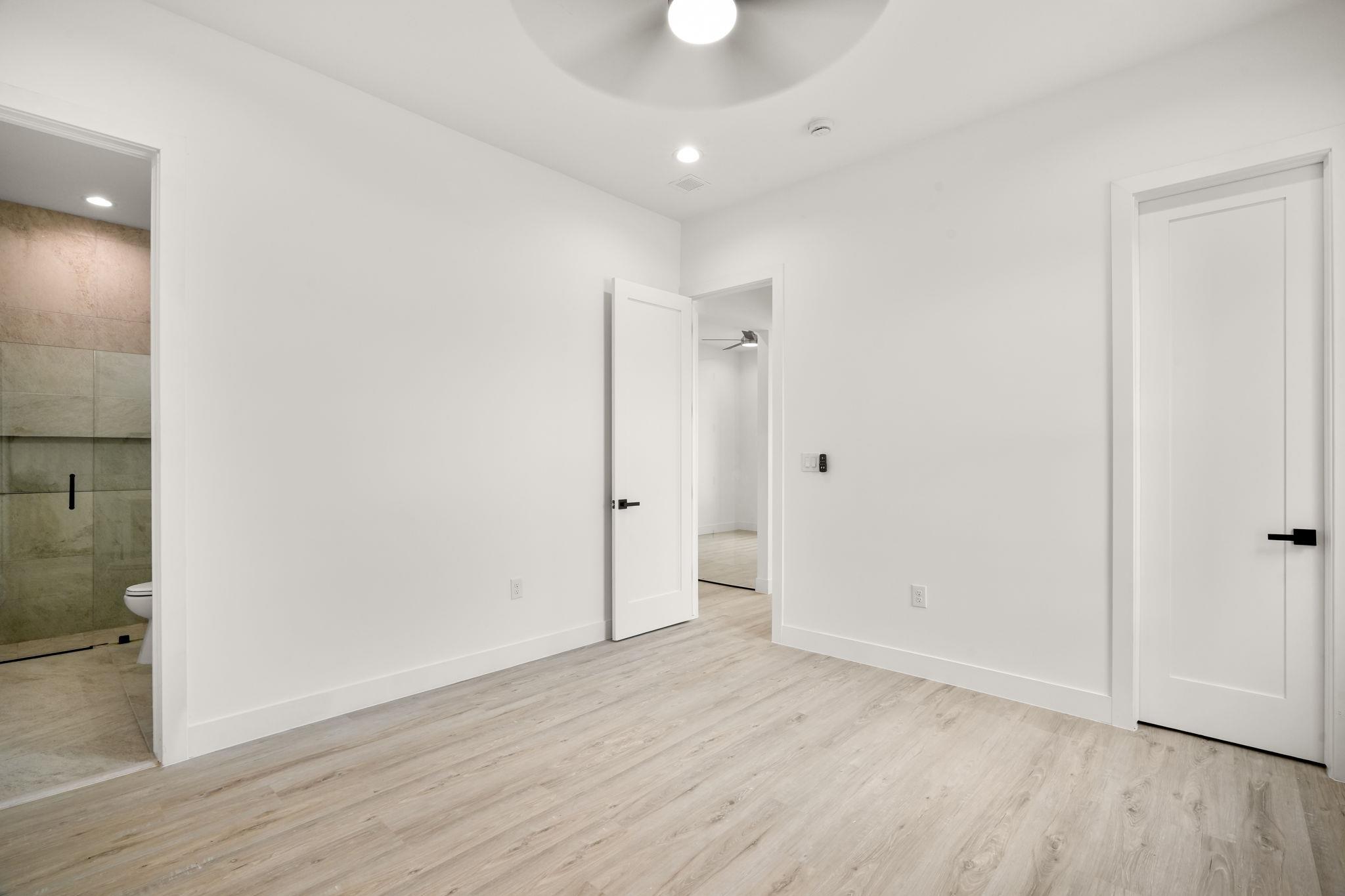 Empty white room with light wood-look floors and a view into a tiled bathroom.
