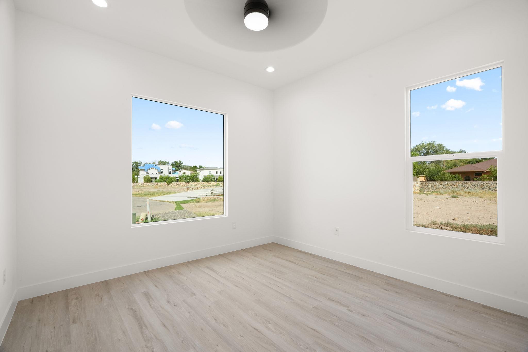 Empty room with light wood-look flooring and two large windows overlooking neighboring homes.