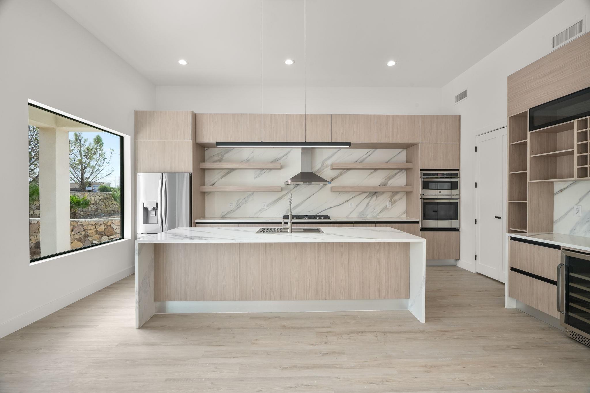 Modern kitchen with pale wood cabinets, marble-look island and backsplash, and stainless steel appliances.