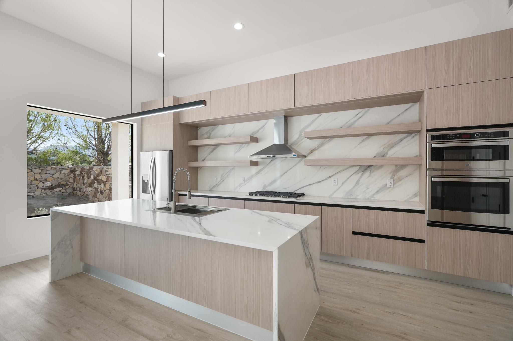 Modern kitchen with a veined marble island, pale wood cabinetry, and stainless steel appliances.