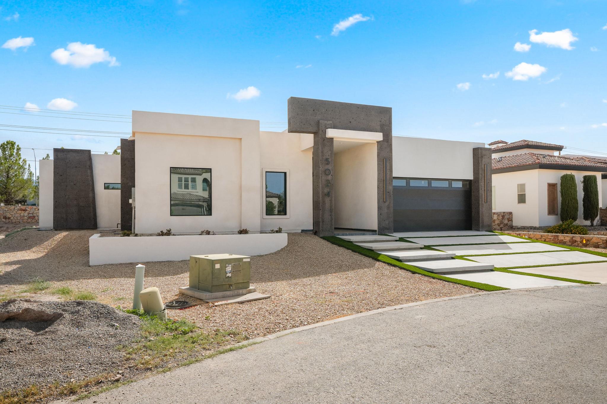 Modern white stucco home with a dark entry surround, attached garage, and grass-lined concrete walkway.