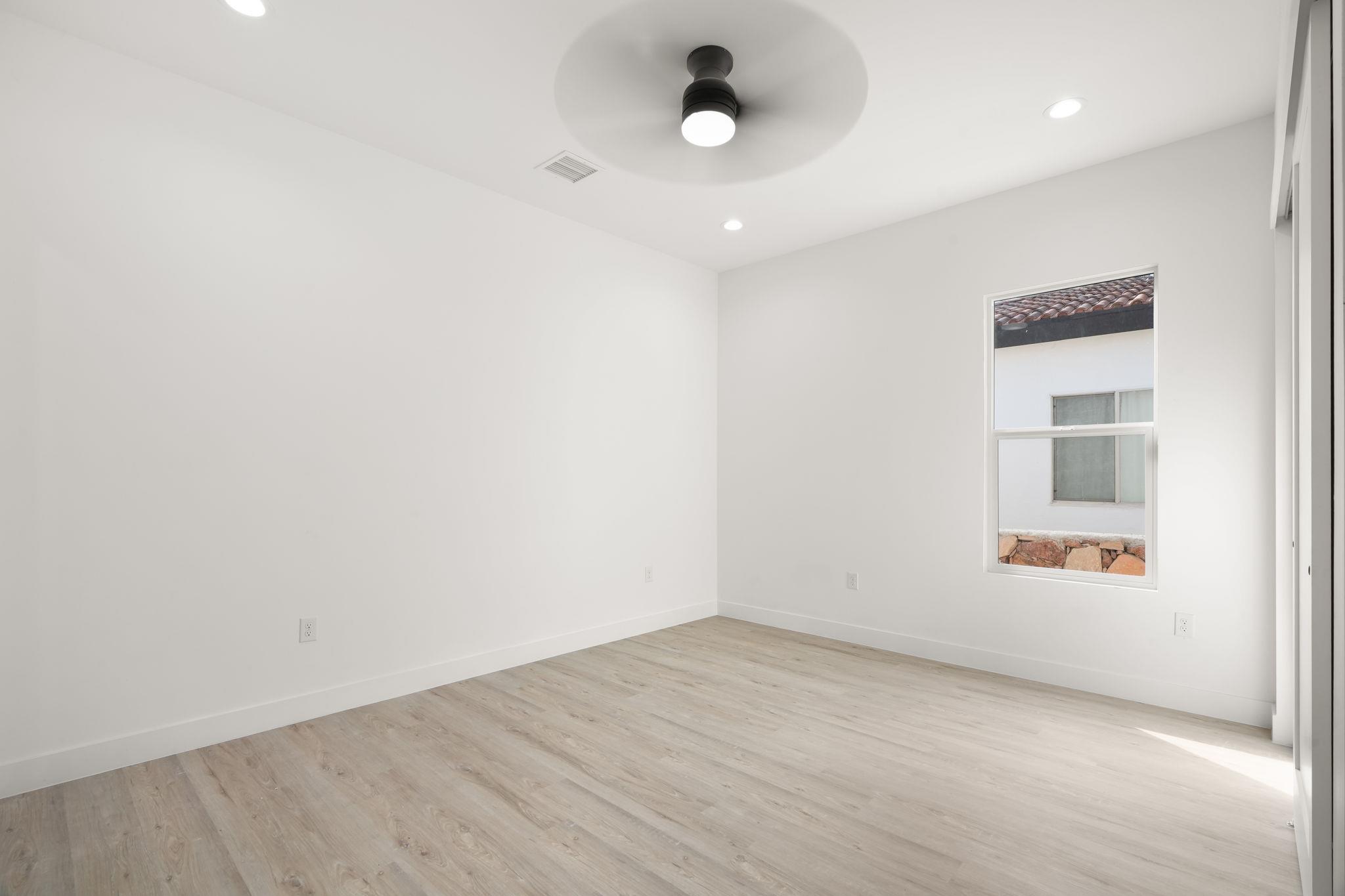 Empty bright room with light wood-look floors, a ceiling fan, and a window.
