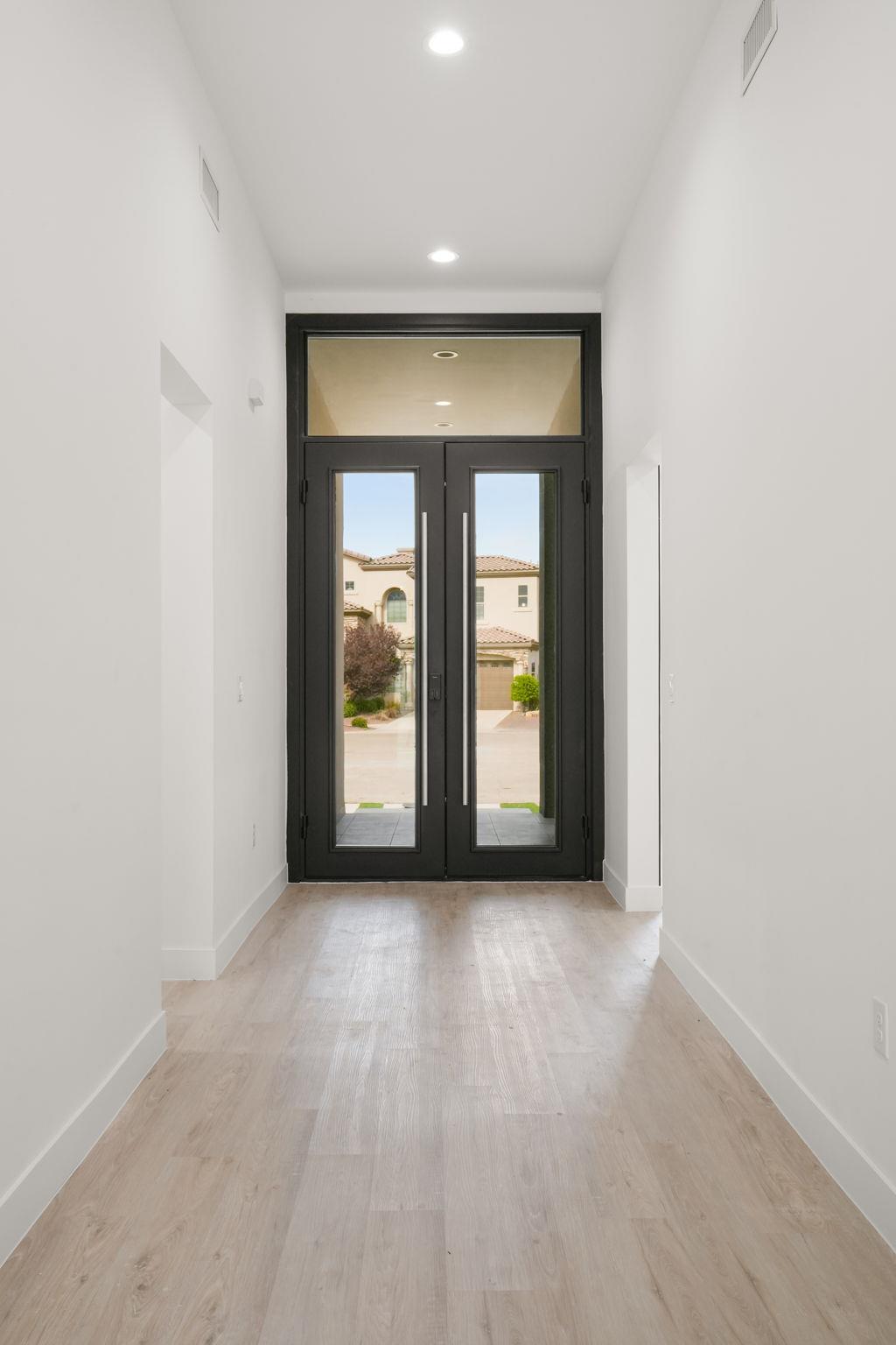 Entry foyer with pale wood floors and tall black double doors with glass panels.