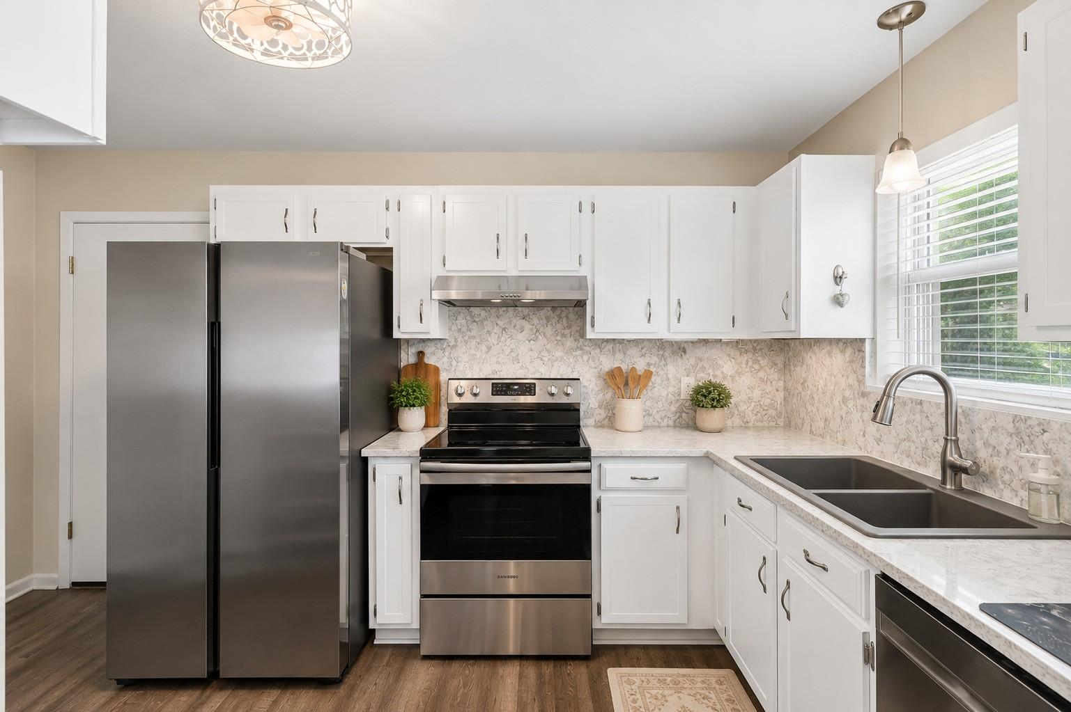 Kitchen with white cabinets, stainless steel appliances, patterned backsplash, and a double-basin sink by the window.