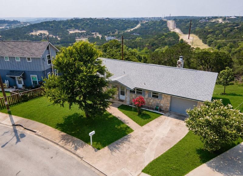 Single-story stone house with a gray roof, front lawn, and curved driveway, viewed from above.