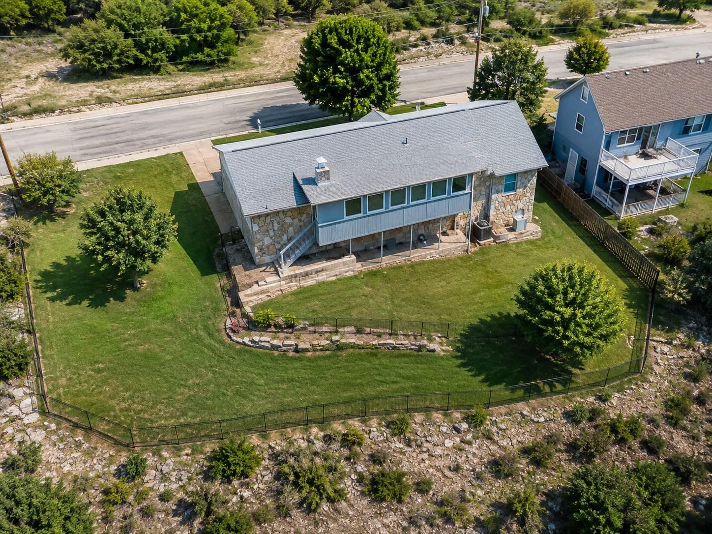 Aerial view of a stone-and-siding home with a large fenced grassy yard.