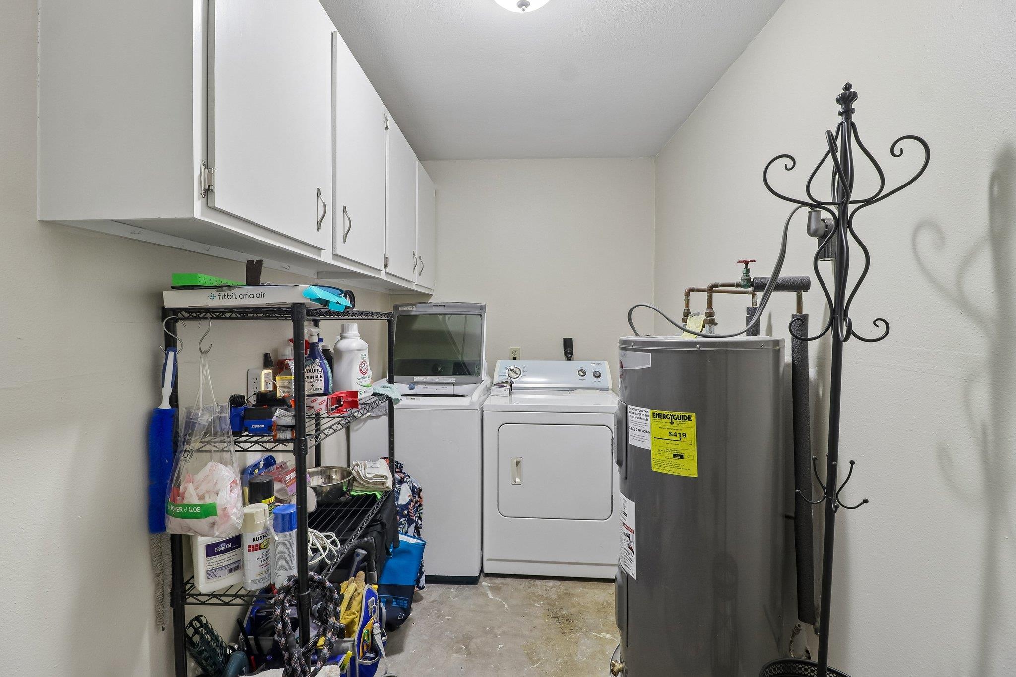 Laundry room with washer and dryer, a large water heater, and storage shelves filled with supplies.