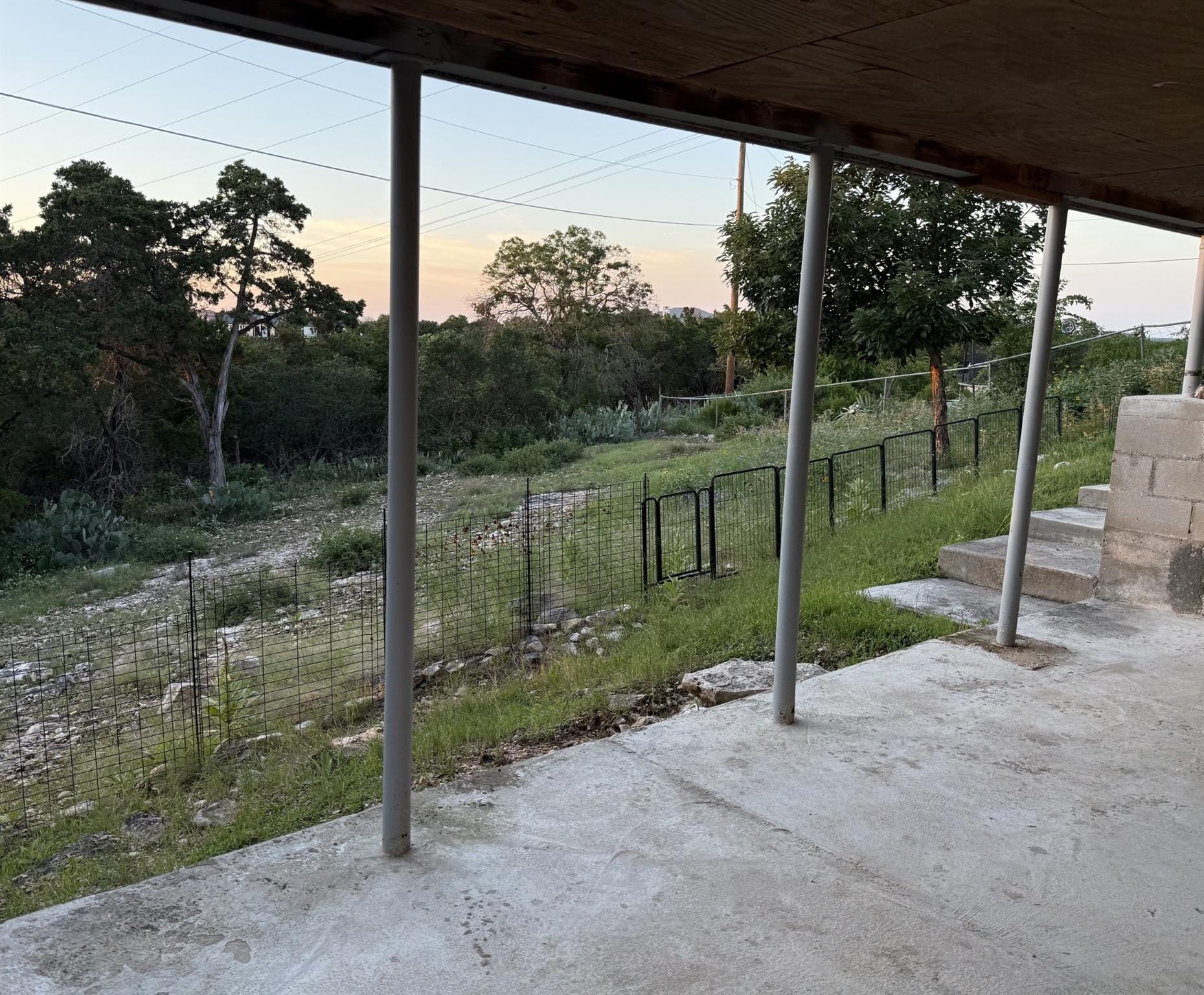 Covered concrete patio overlooking a fenced, grassy yard with native trees.