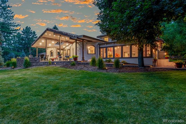 Modern home with a warmly lit covered patio and broad lawn at dusk.